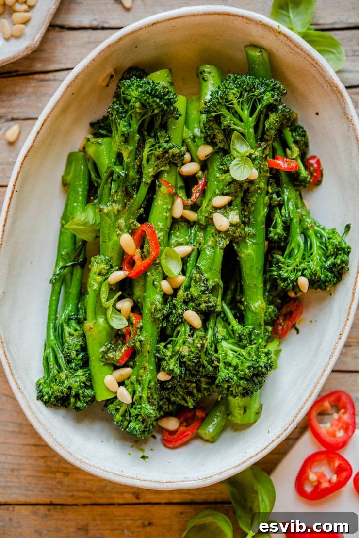 Sauteed Broccolini with Pesto, Pine Nuts and Chilli. This simple vegetable side dish is packed with flavour with pesto, chili and crunchy pine nuts. Serve this broccolini with roast meats, fish or salad for a complete meal. | Italian Sides | Healthy Sides | Broccoli Sides | #broccolini #sides #broccoli A close up of vibrant green sauteed broccolini in a serving bowl, garnished with golden pine nuts and red chili flakes.