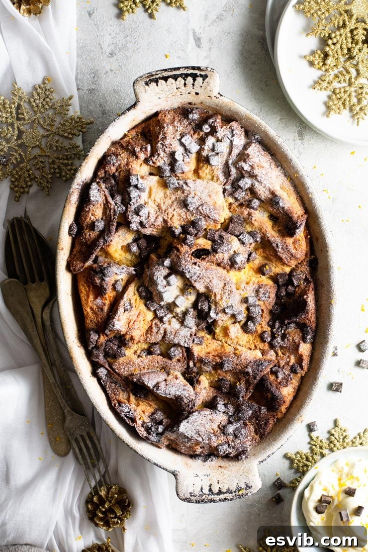 Panettone Bread Pudding: A Delicious Italian Christmas Dessert with Festive Spices and Chocolate Chips, Easy and Comforting, Perfect with Fresh Whipped Cream. An overhead shot of golden panettone bread pudding in an oval baking dish, adorned with powdered sugar and melted chocolate chunks, with a side of fresh whipped cream, ready to be served as a delightful and comforting Christmas dessert.