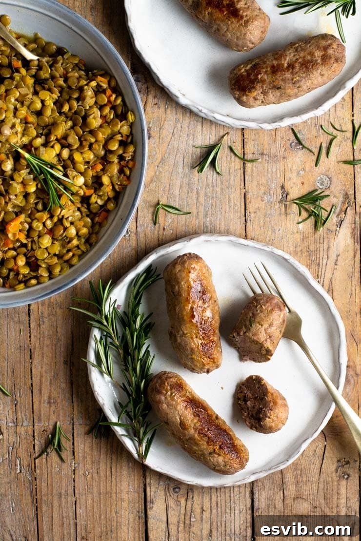 Homemade Italian sausages resting on a plate, surrounded by fresh rosemary and a bowl of rustic lentils, ready to be served.