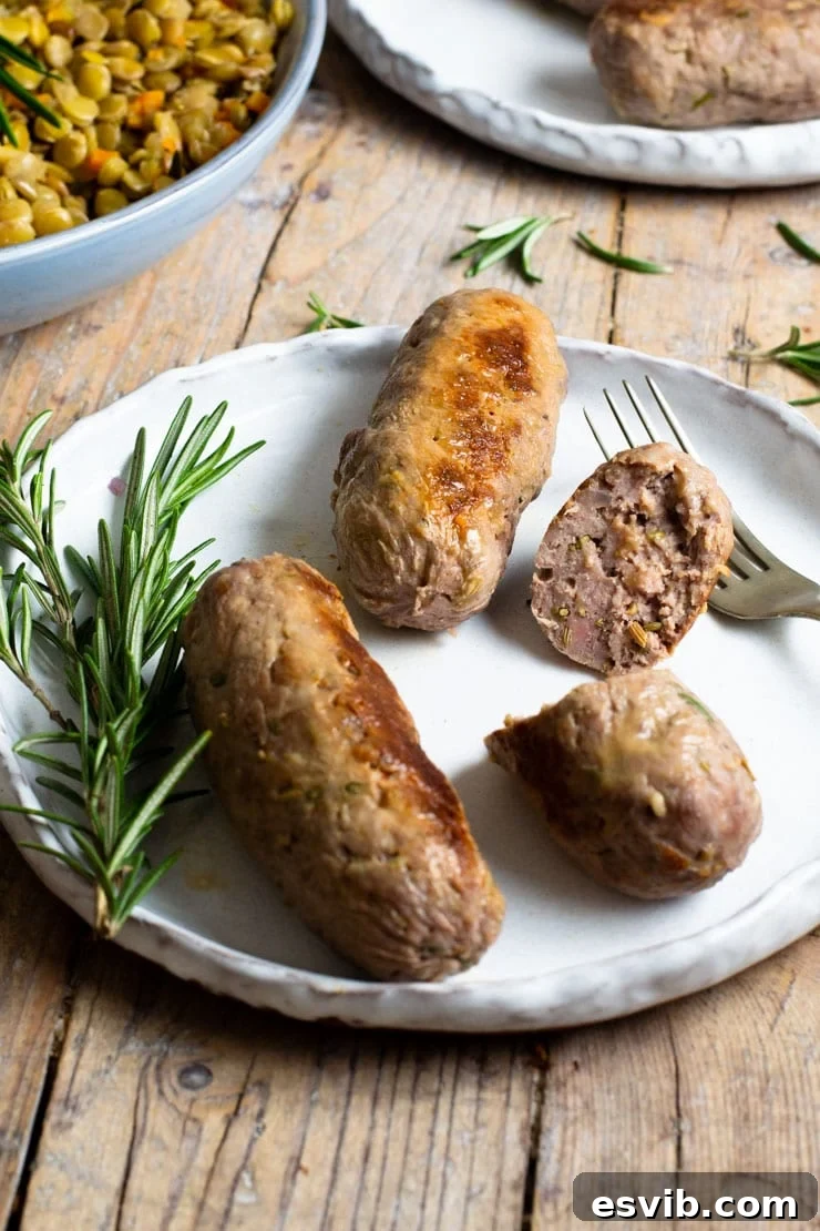 Three perfectly cooked homemade Italian sausages on a white plate, one sliced in half to reveal its juicy interior, garnished with fresh rosemary sprigs for an appealing presentation.