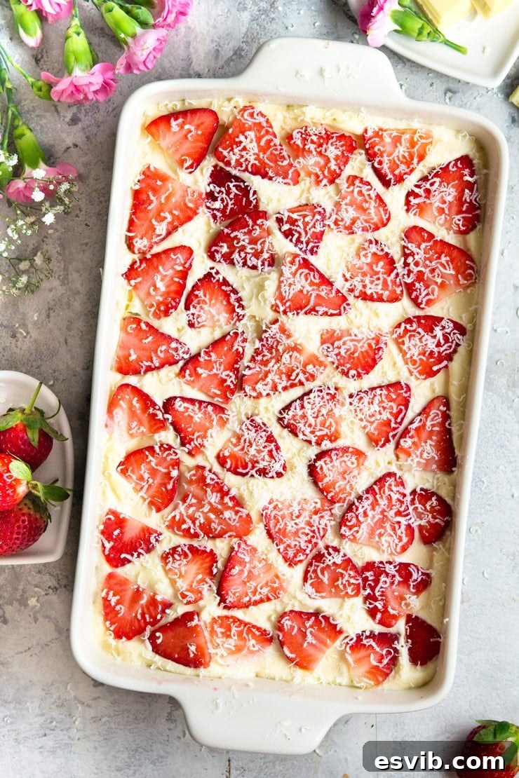 An overhead shot of a rectangle dish filled with layers of creamy strawberry tiramisu, garnished with fresh strawberry slices and white chocolate shavings.