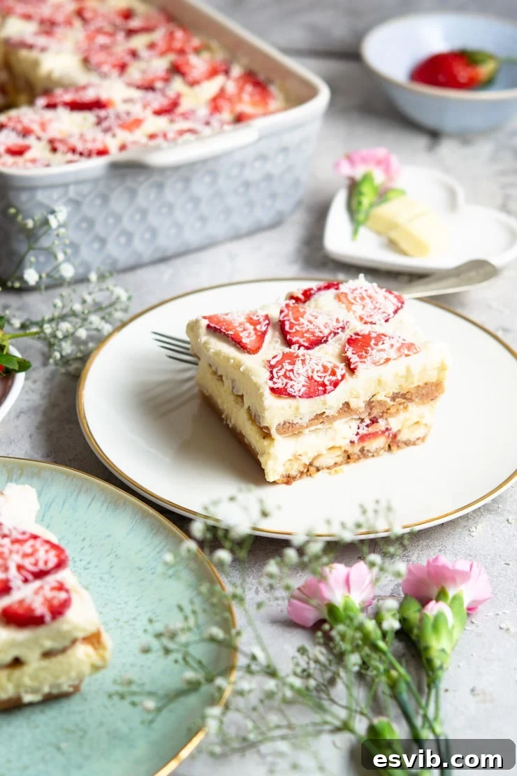 A beautiful slice of strawberry tiramisu on a white plate, garnished with fresh strawberry slices and white chocolate, with delicate flowers scattered around.