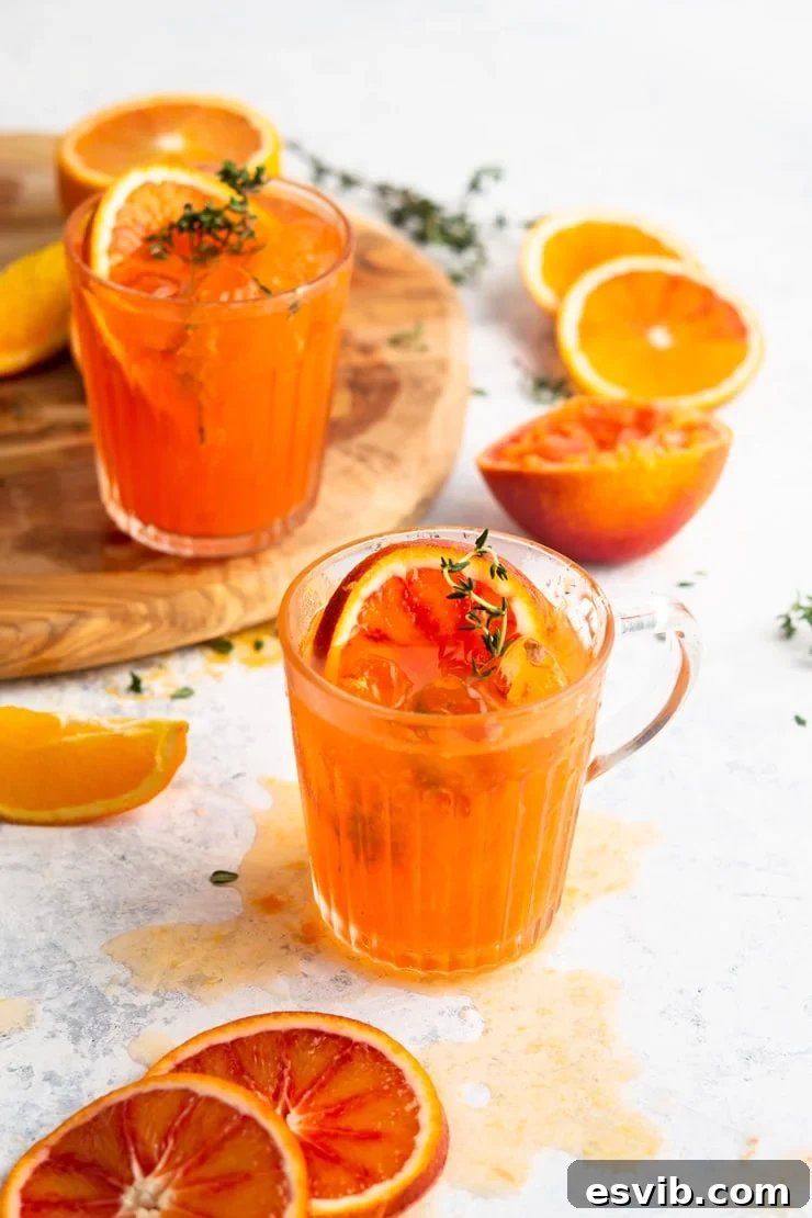 Vibrant Blood Orange Gin Cocktail garnished with thyme and fresh orange slices, set against a rustic background.