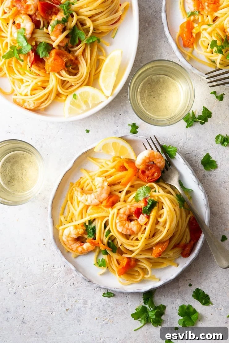 A beautifully presented plate of shrimp linguine, adorned with vibrant burst cherry tomatoes, generous fresh parsley, and bright lemon wedges, with elegant glasses of white wine in the background. This image highlights a quick and easy Italian seafood pasta recipe.