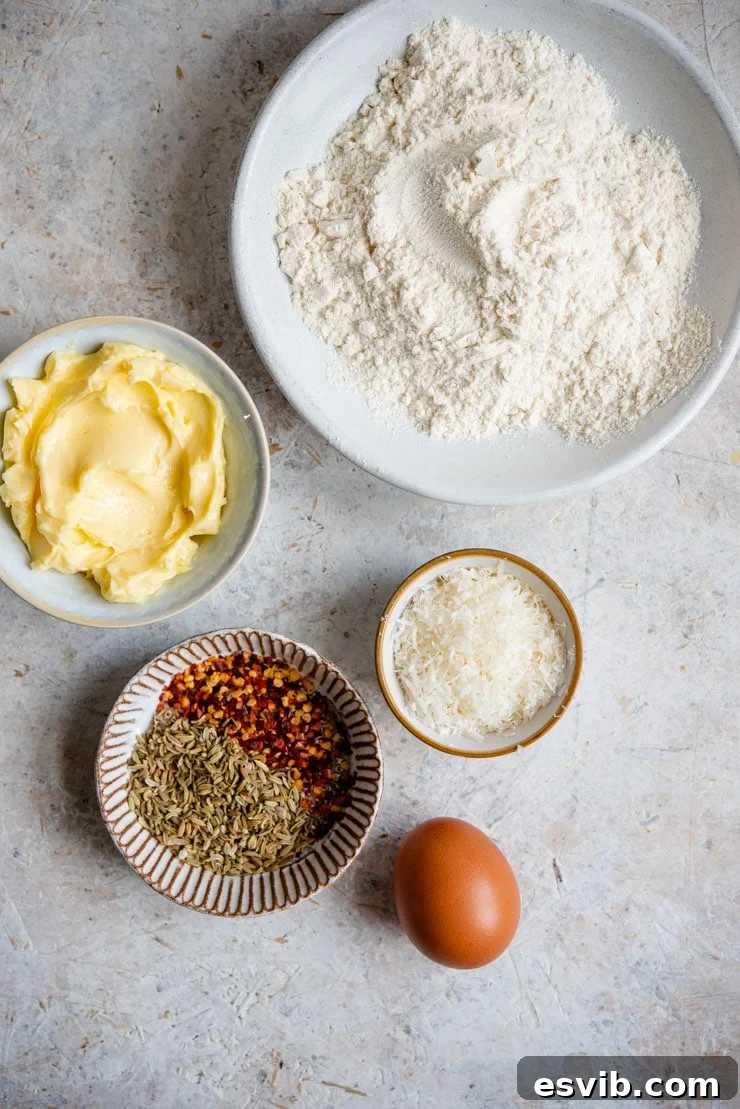 Ingredients for Parmesan Cheese Cookies An overhead shot showcasing all the essential ingredients laid out for making Parmesan Cheese Cookies: a bowl of flour, softened butter, freshly grated Parmesan, an egg, and small bowls of red pepper flakes and fennel seeds.