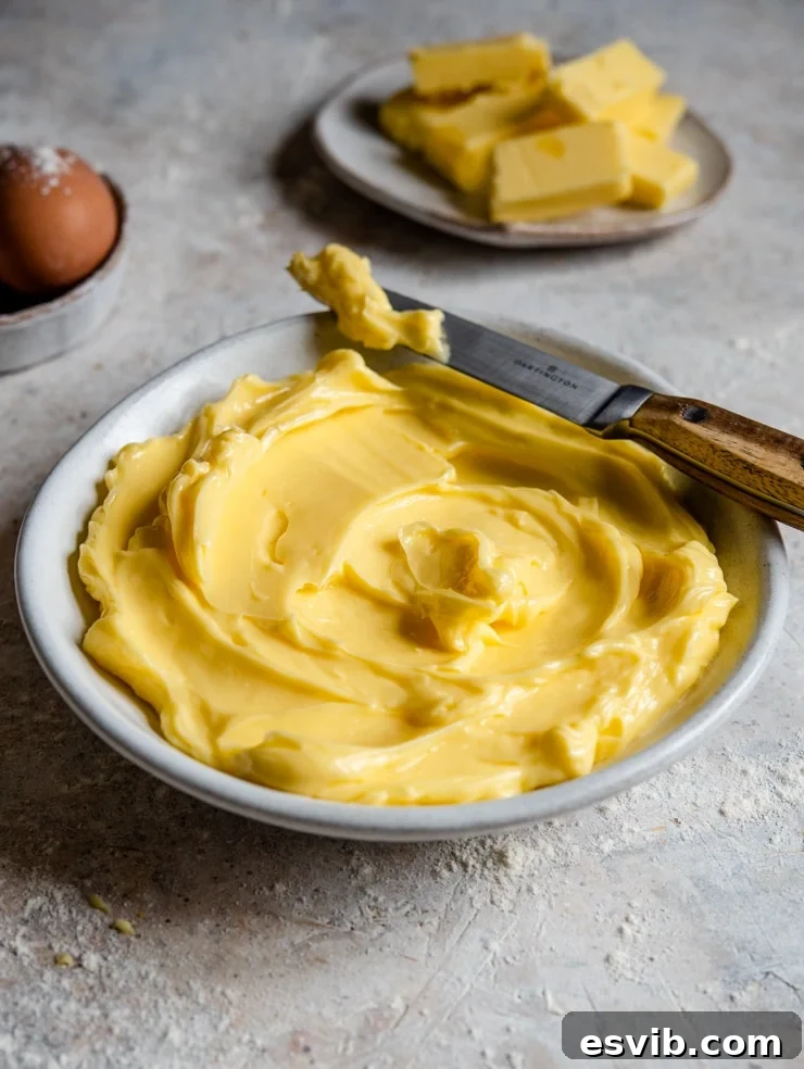 Quick Butter Softening Method for Baking A side shot of perfectly softened butter in a bowl with a knife, demonstrating its creamy, pliable texture.