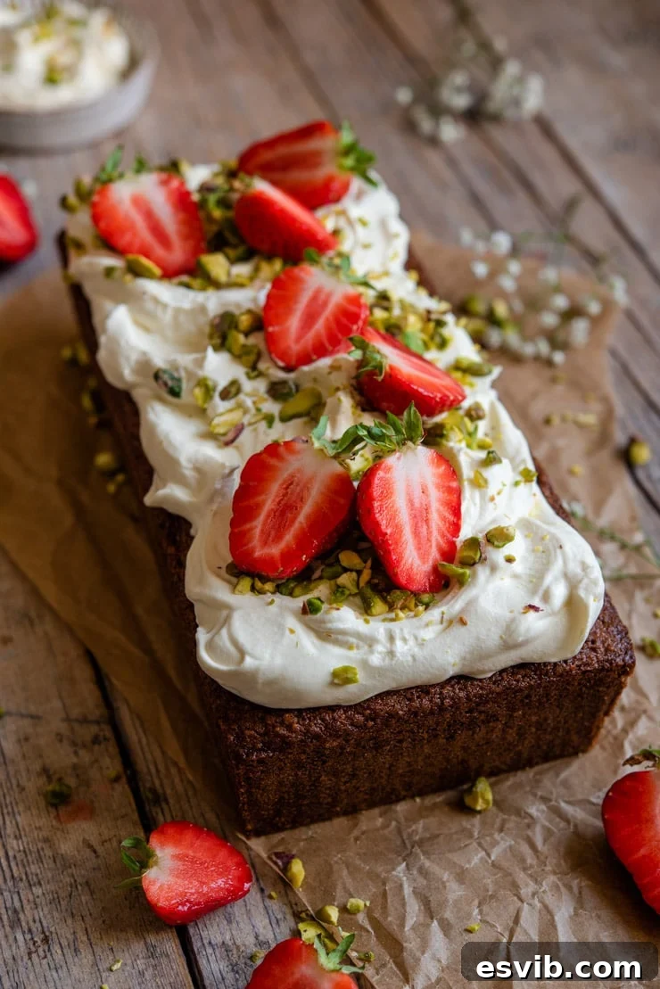 A close-up side view of a pistachio cake, generously topped with whipped cream and fresh sliced strawberries, highlighting its moist texture