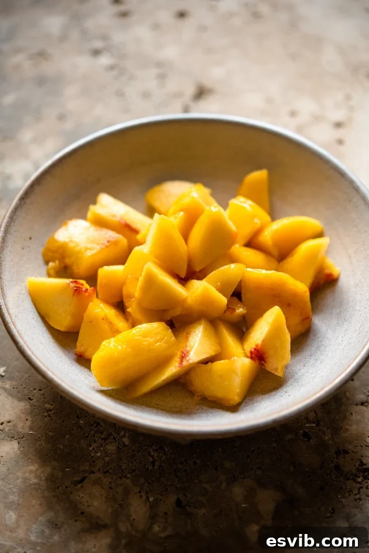 Freshly chopped ripe peaches resting in a clear glass bowl, showcasing their vibrant color and readiness to be blended into a smooth, flavorful puree for cocktails.