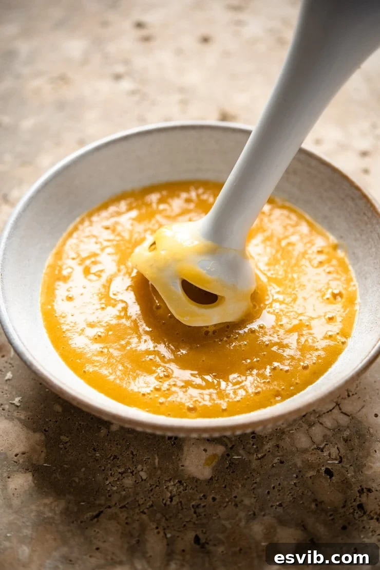 A close-up shot of the process of making peach puree for a Bellini cocktail, showing the vibrant texture of blended fresh peaches in a bowl.