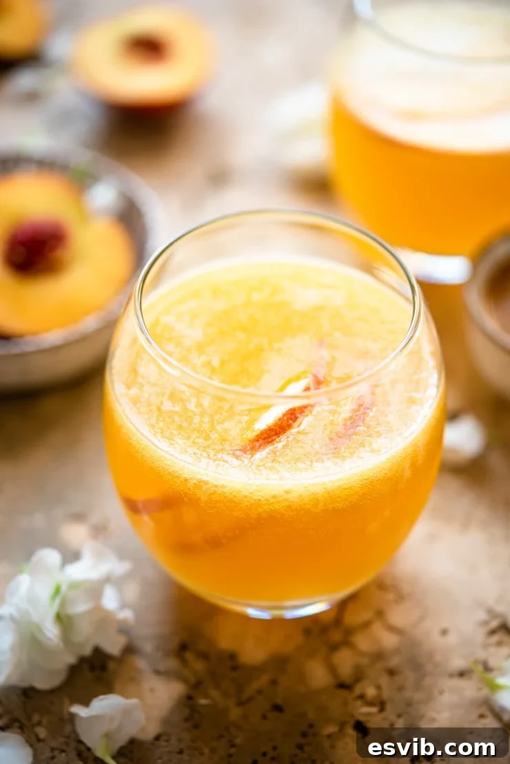 A close-up of a perfectly poured Peach Bellini cocktail in a delicate, round stemless glass, highlighting its beautiful peachy hue and gentle bubbles.