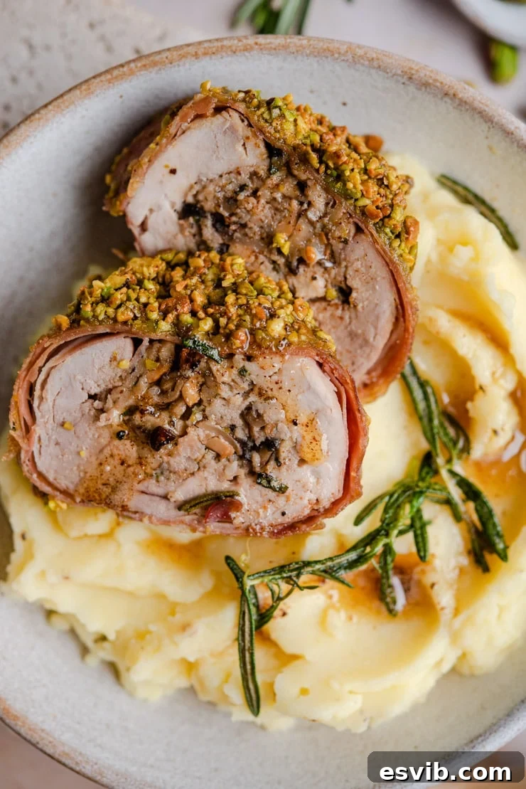 A close-up shot of a perfectly cooked slice of Stuffed Pork Tenderloin resting on a bed of creamy mashed potatoes, garnished with fresh herbs.