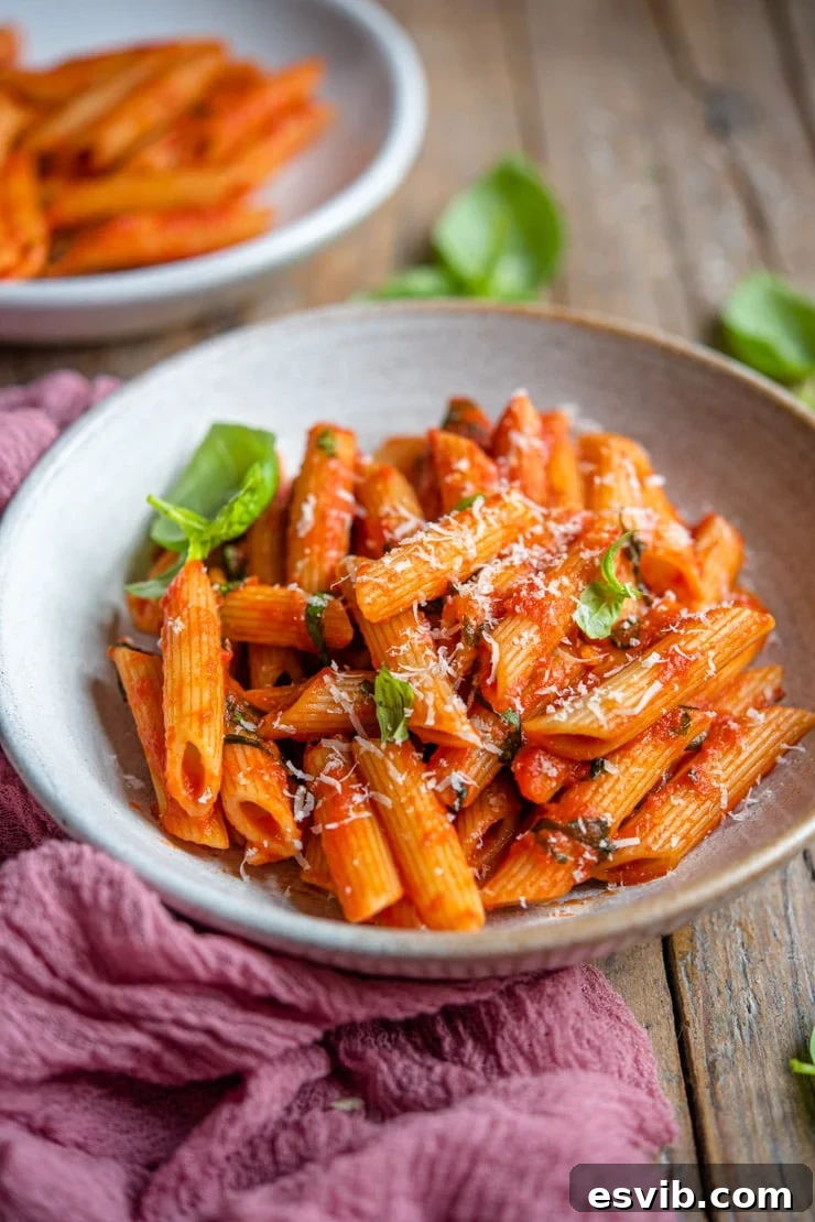 A side shot of penne pomodoro in a rustic bowl, showing off the rich sauce and basil