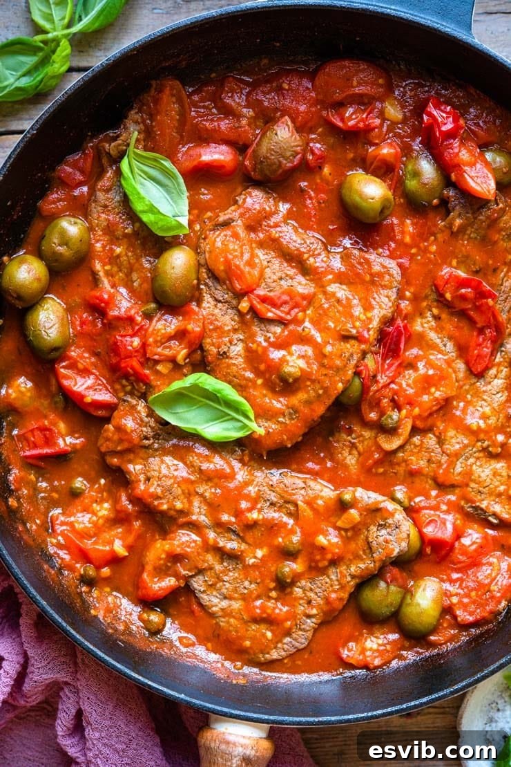 Delicious Steak Pizzaiola in Skillet Ready to Serve A close-up view of the finished Steak Pizzaiola in a skillet, showcasing the rich tomato sauce, olives, and tender steak, garnished with fresh basil