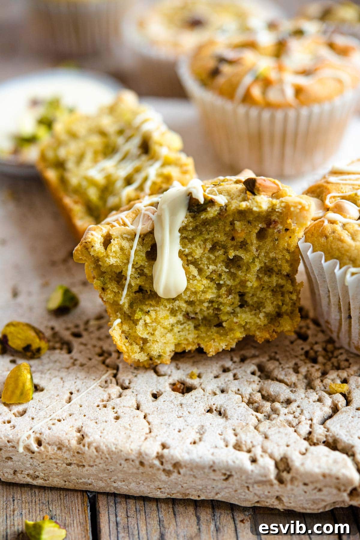 Emerald & Ivory Muffins 5 A close up of a pistachio muffin cut in half with melted white chocolate drizzled on top, revealing the moist interior.
