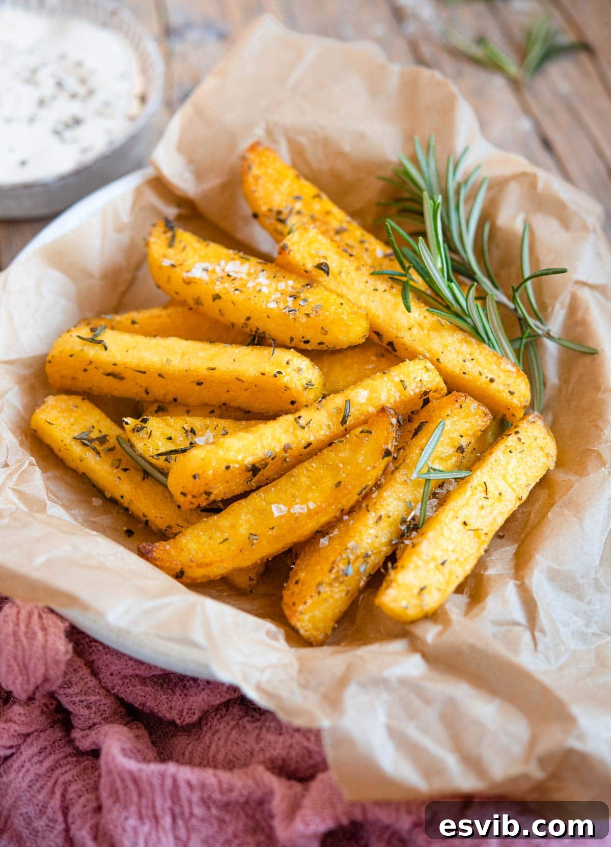 A side shot of a bowl filled with golden-brown polenta fries, garnished with fresh rosemary sprigs.