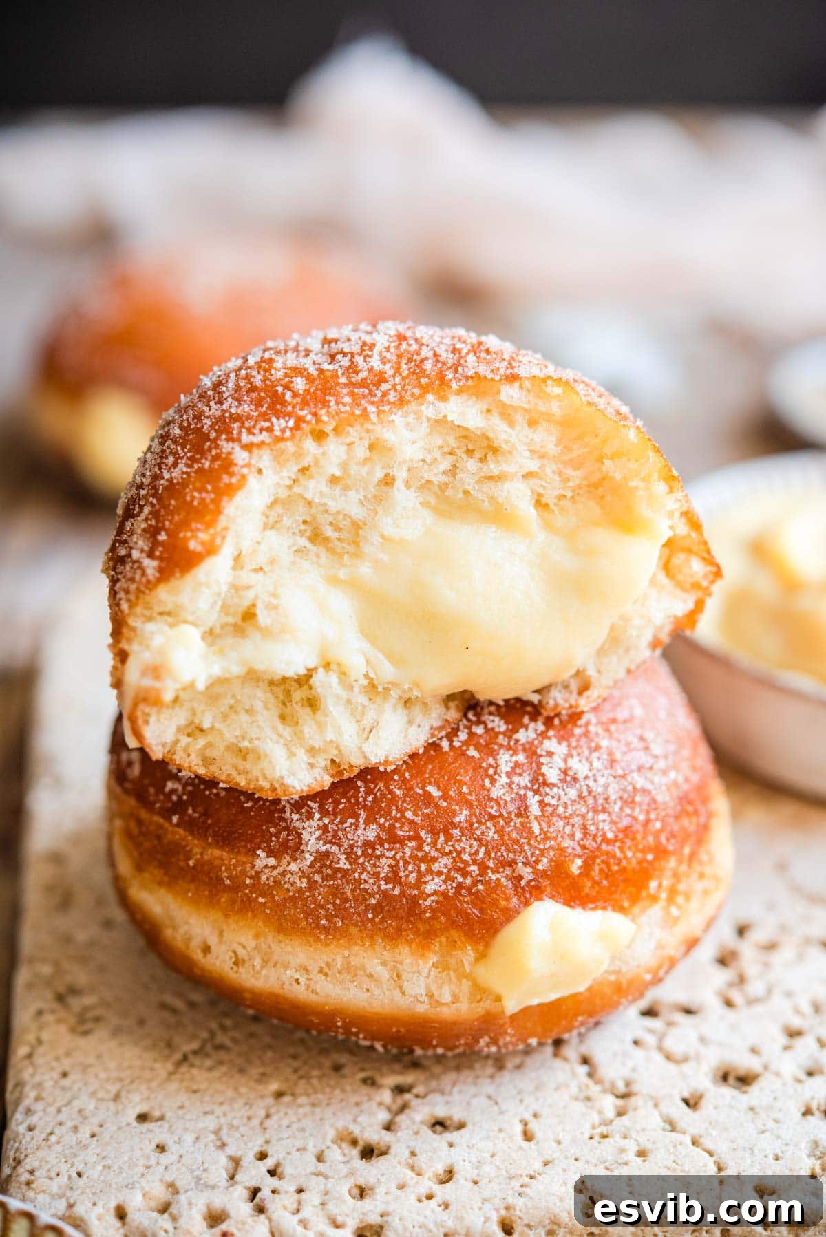 Bomboloni Italian Fried Pastry Bliss 12 Two soft bomboloni doughnuts stacked, with one cut in half to show its luscious cream filling and light interior.