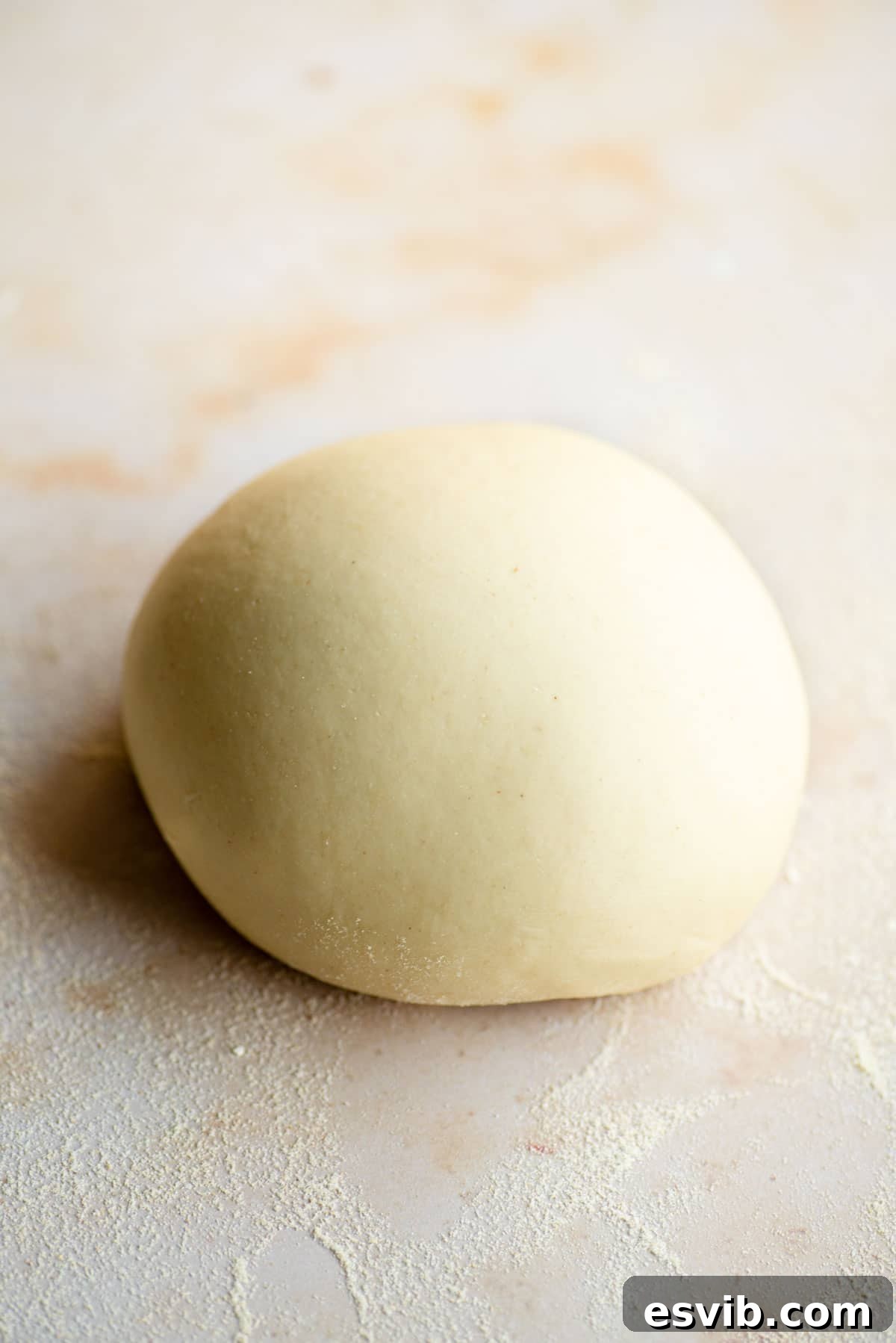 A perfectly kneaded ball of golden semolina pasta dough resting on a light marble surface, ready for shaping.