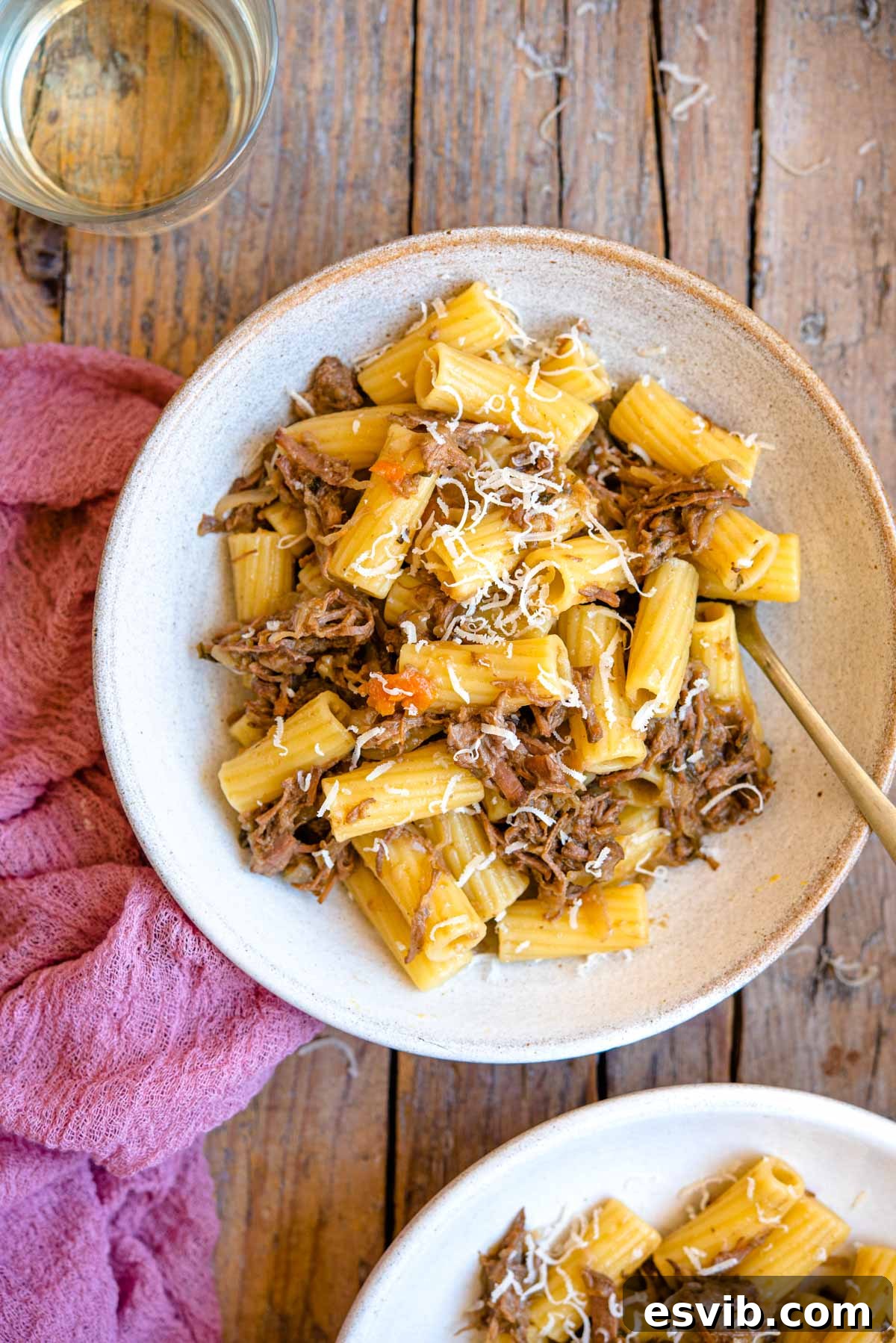 An overhead shot of Genovese sauce with rigatoni pasta in a bowl with a glass of wine beside it