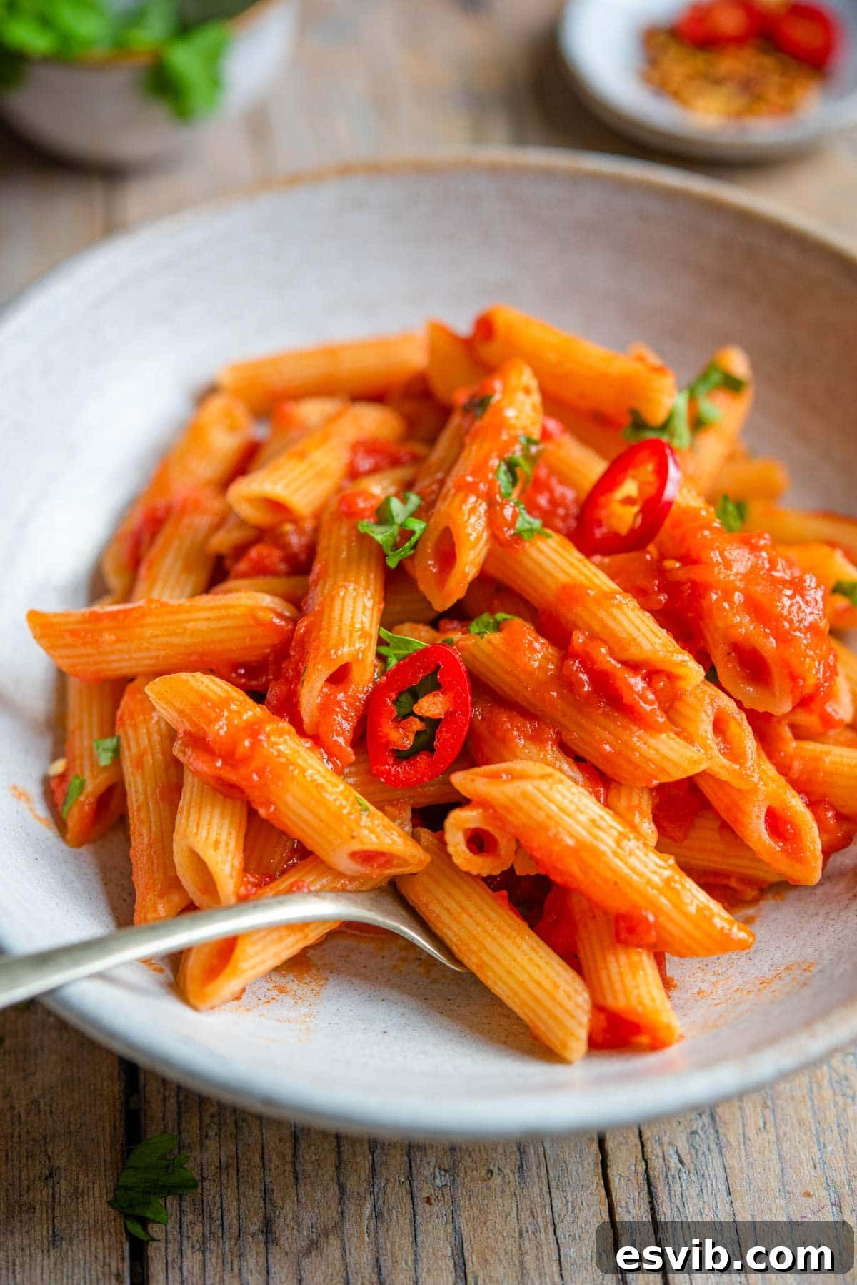 A close up shot of Penne all' Arrabbiata in a rustic bowl, with a fork twirled into the pasta, ready to eat and garnished with fresh herbs