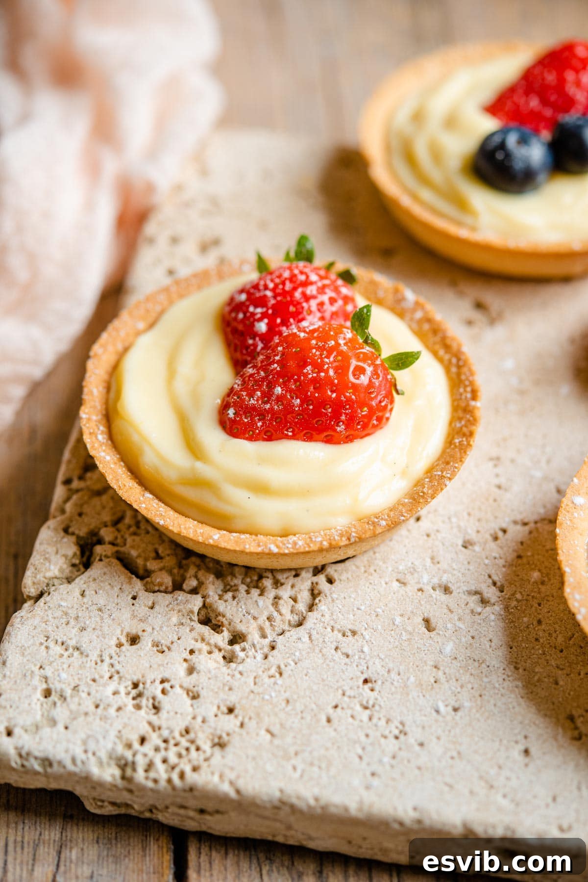 Velvety Italian Custard Cream 2 A small individual sized pie crust filled with Italian pastry cream and topped with two slices of strawberry. The cream is smooth and yellow.