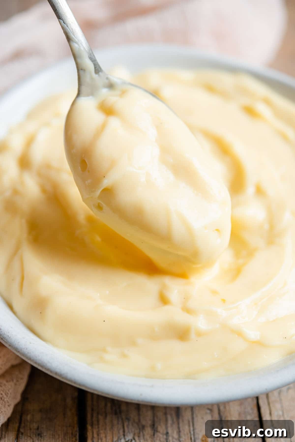 Velvety Italian Custard Cream 7 A close up shot of a spoonful of glossy, yellow Italian pastry cream, demonstrating its smooth and creamy texture.