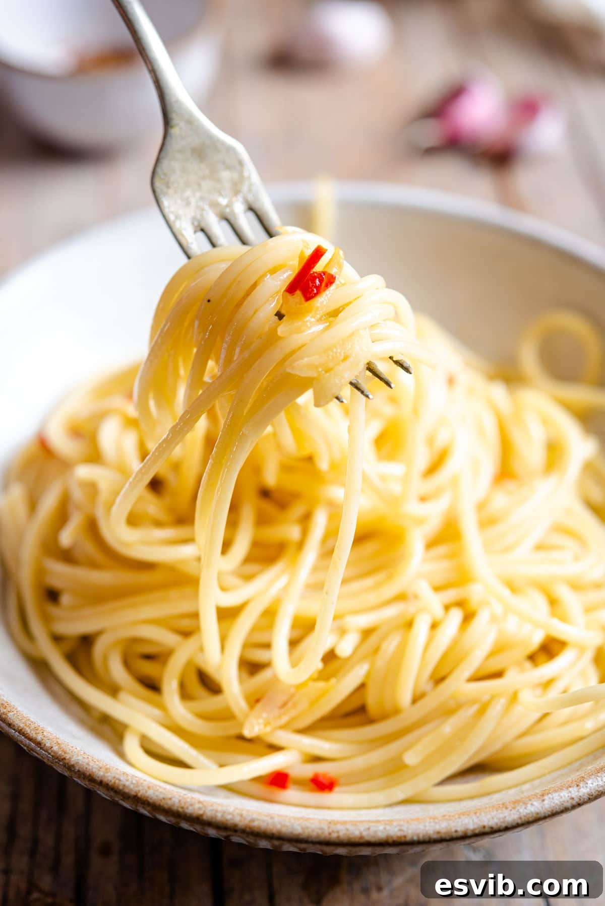 Spaghetti Aglio e Olio: Golden Garlic and Olive Oil Delight 4 A close-up shot of spaghetti twirled on a fork, garnished with chili and garlic slices.