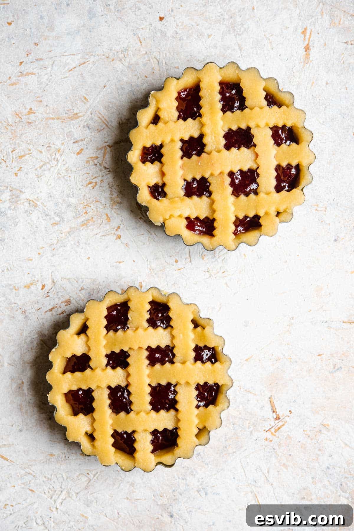 An overhead shot of two unbaked shortcrust pastry tarts, one with a lattice top and one with a solid base.
