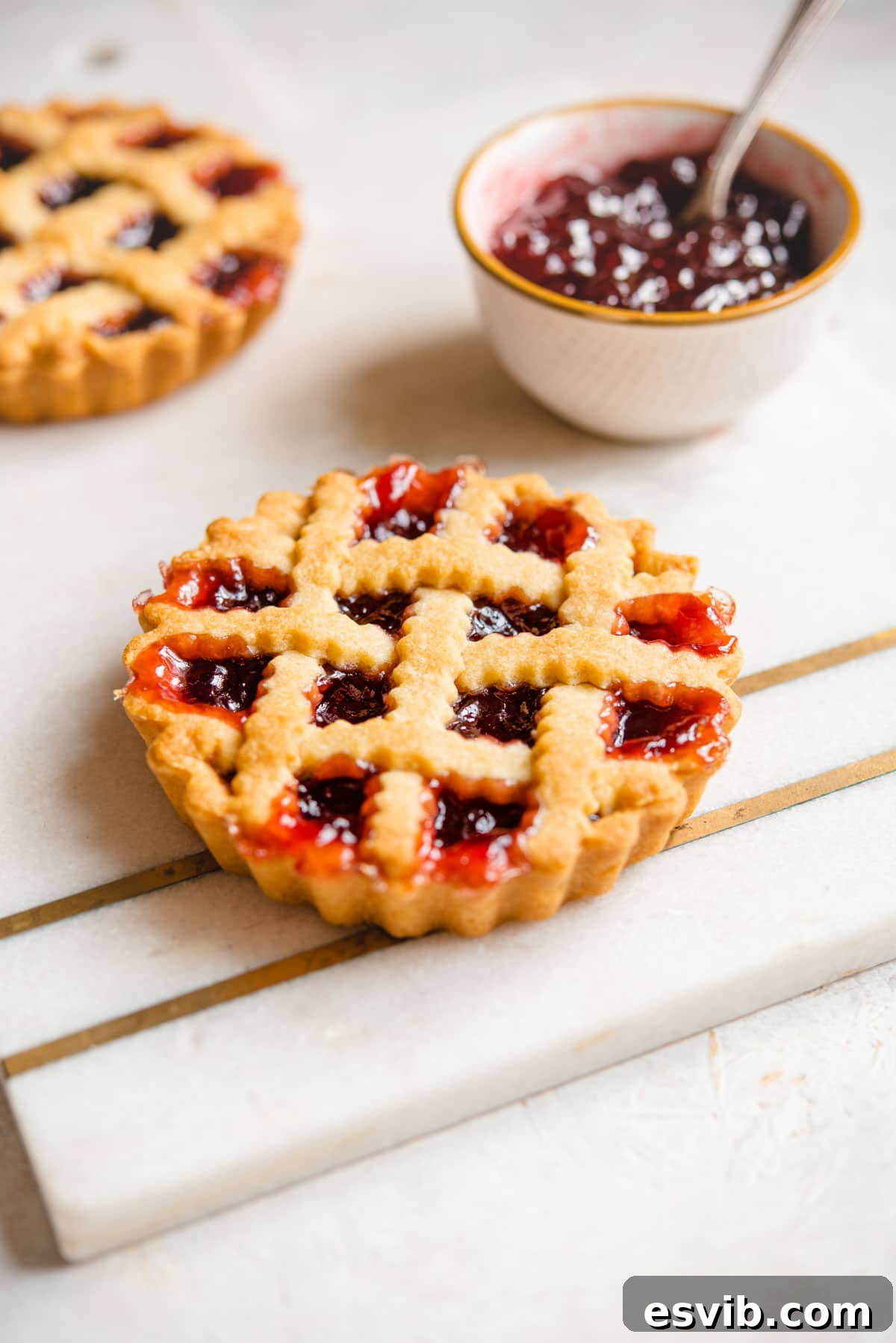 A mini Italian jam tart with a lattice top, served on a marble cutting board.