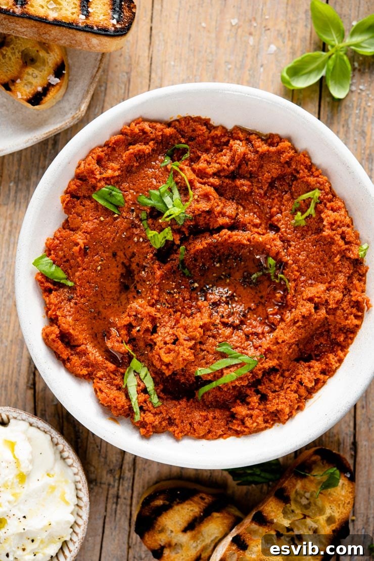 A bowl of rich red pesto, garnished with fresh basil, next to slices of bread ready for spreading.