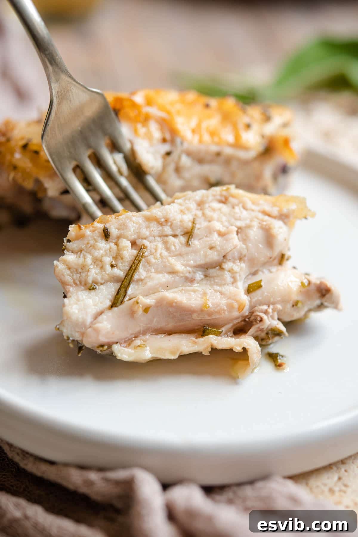 Tuscan Herb Roasted Chicken Thighs 5 A close up of a juicy piece of Italian baked chicken thigh on a fork, showing its tender interior and crispy skin.