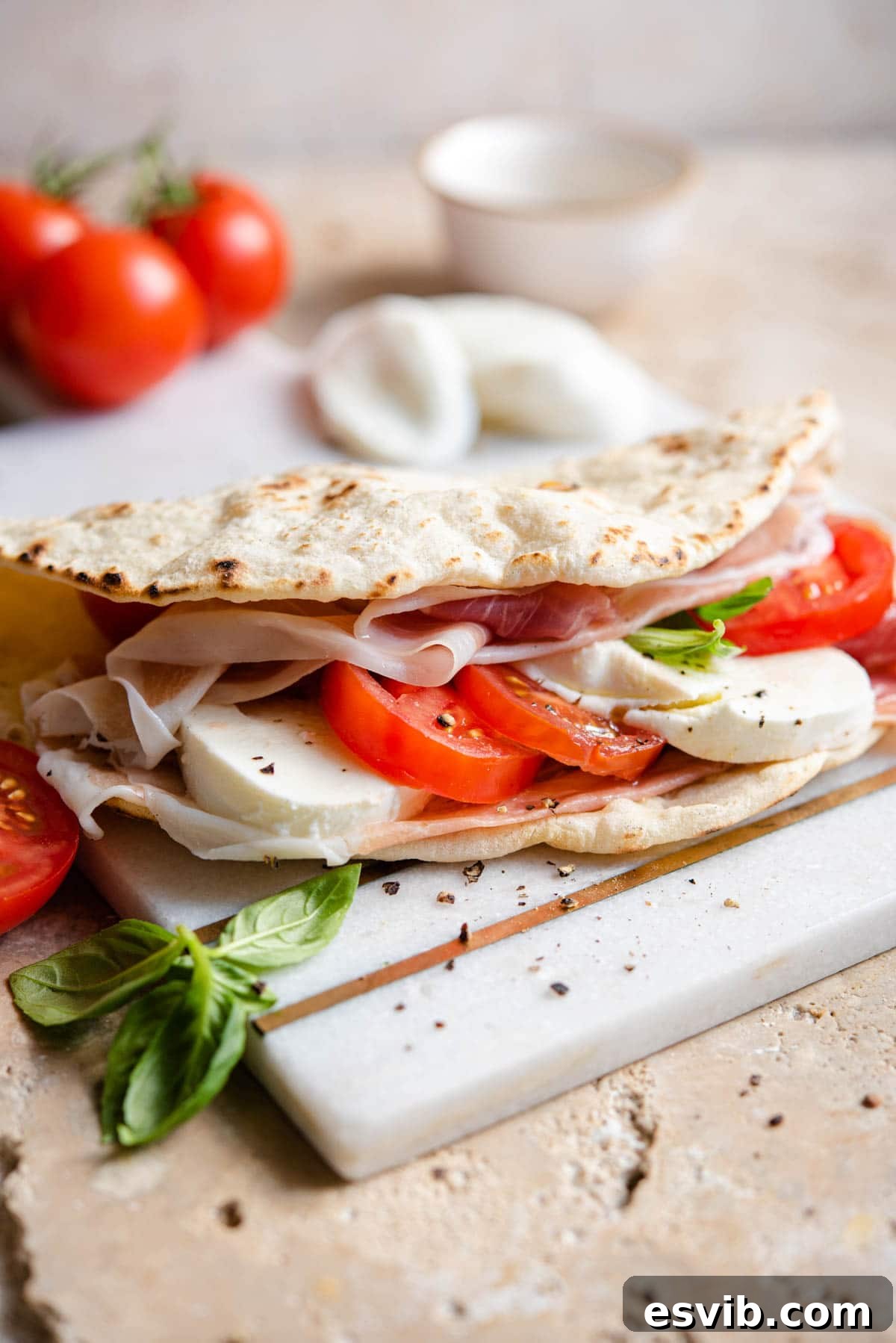 Piadina: Italy's Signature Flatbread 2 A Piadina flatbread stuffed with tomatoes, mozzarella and prosciutto sitting on a marble board, highlighting its soft texture and generous filling.