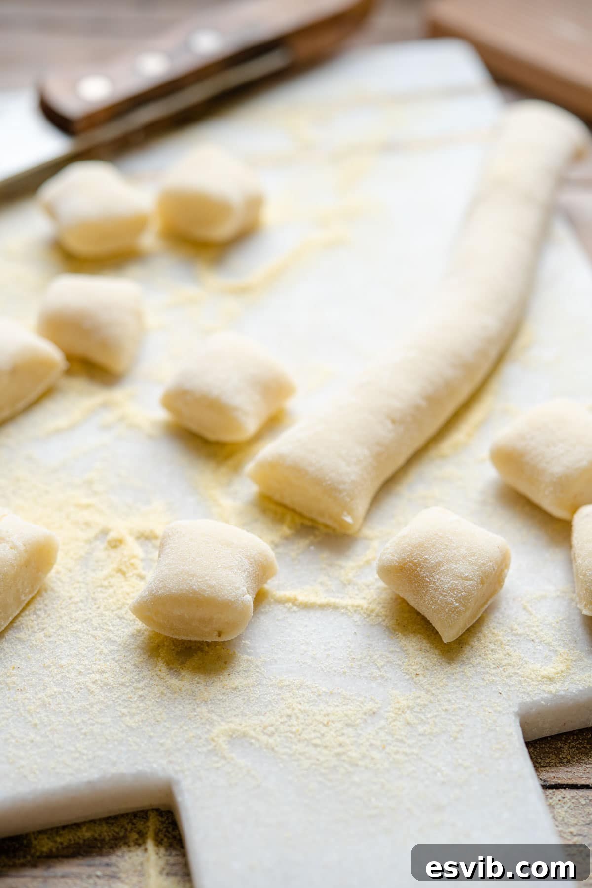 A close-up, artful shot of perfectly shaped potato gnocchi, unadorned and ready for cooking, resting on a rustic wooden cutting board, emphasizing their soft, inviting texture.