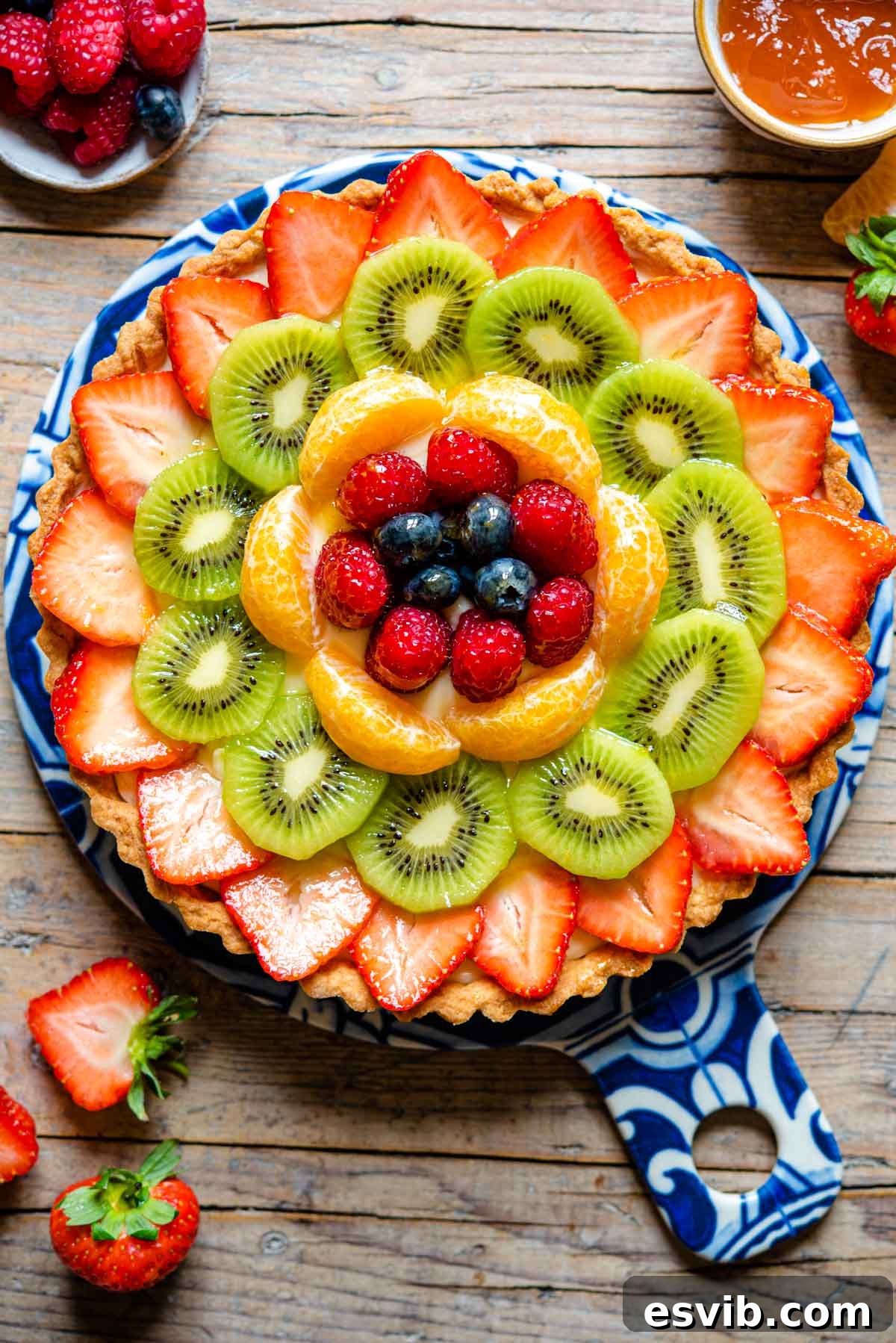 An overhead shot of a perfectly baked Italian fruit tart, Crostata di Frutta, filled with creamy vanilla pastry cream and topped with an assortment of colorful fresh fruits and a glossy apricot glaze.