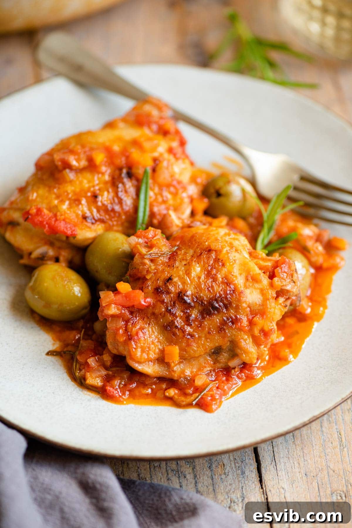 Rustic Hunter's Chicken 7 Two chicken thighs on a plate with a tomato and vegetable sauce and olives