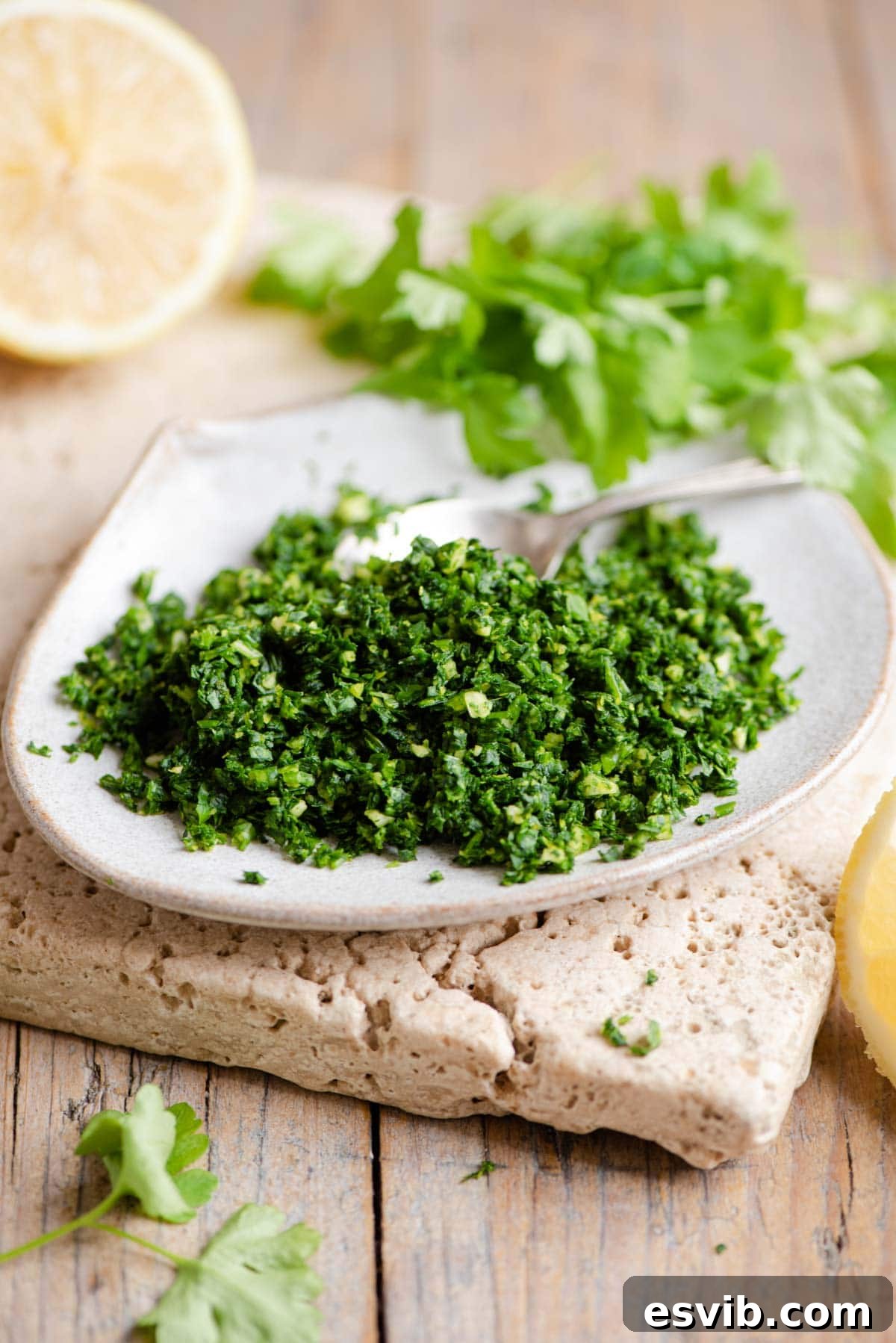 Zesty Italian Herb Gremolata 2 Freshly made Gremolata on a small white plate, garnished with lemon wedges and fresh parsley in the background, highlighting its vibrant green color.