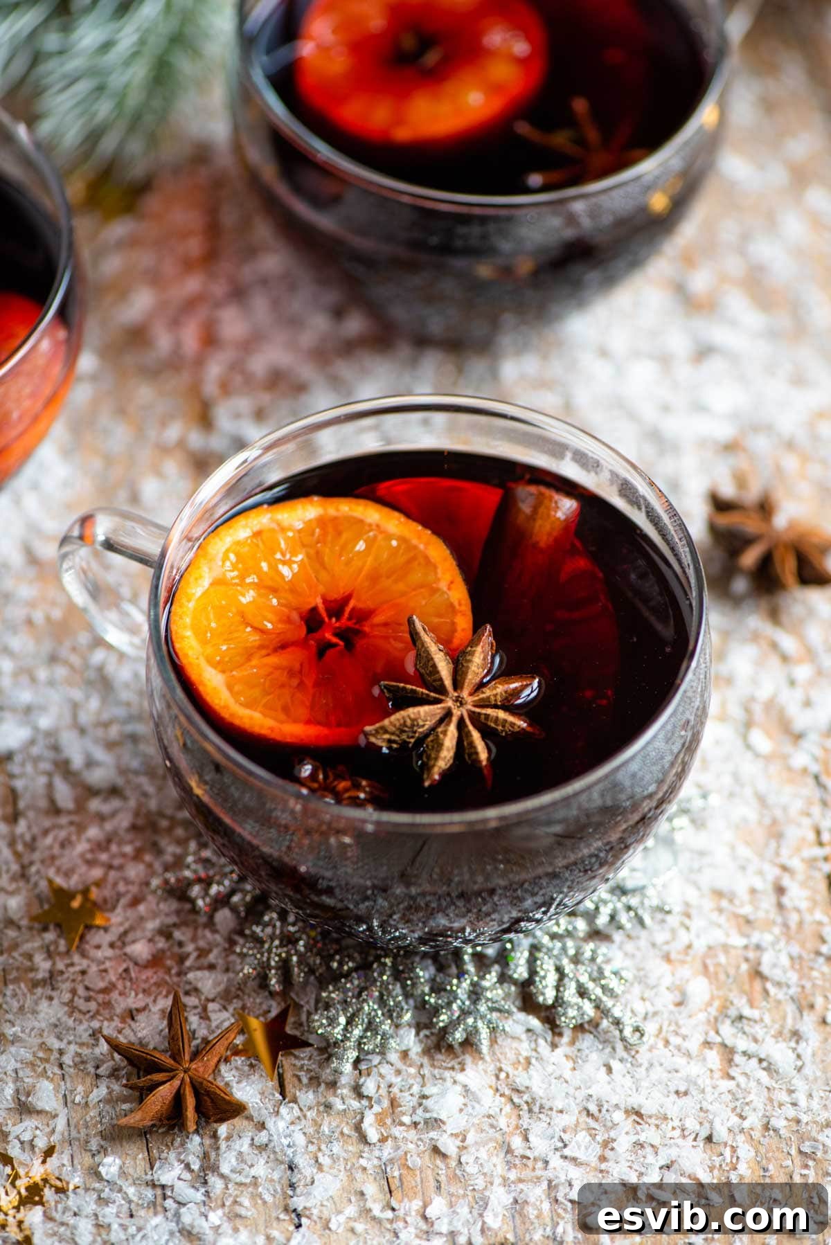 A mug of mulled wine on a snowy wooden surface, garnished with clementine slice and star anise