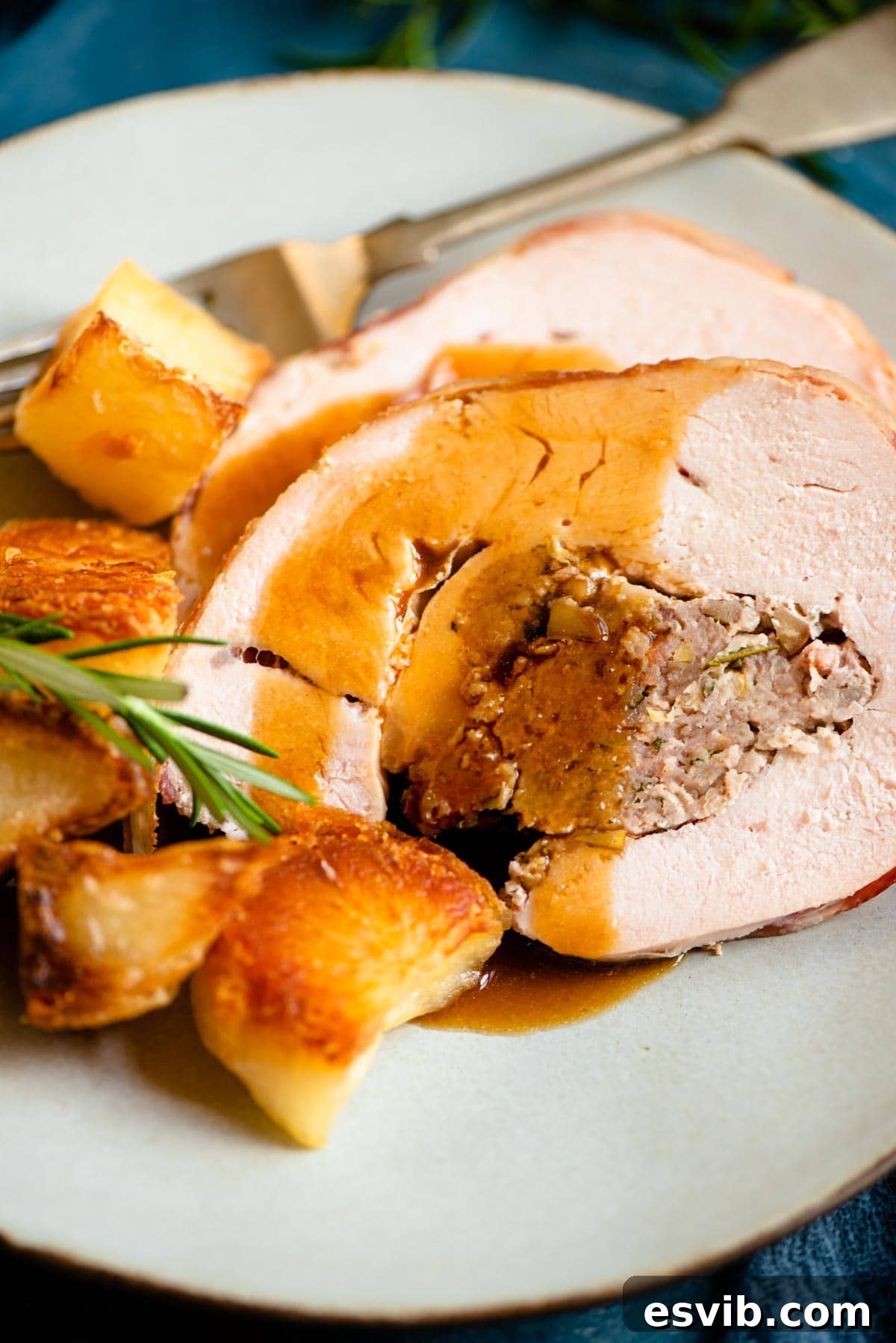 A close-up of beautifully carved slices of Sausage & Chestnut Stuffed Turkey Breast, artfully arranged on a plate with rich brown gravy pooling around them, ready to be served.