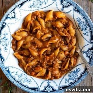 Pasta and lentils in a blue and white vintage bowl sitting on a wooden surface, ready to be enjoyed.