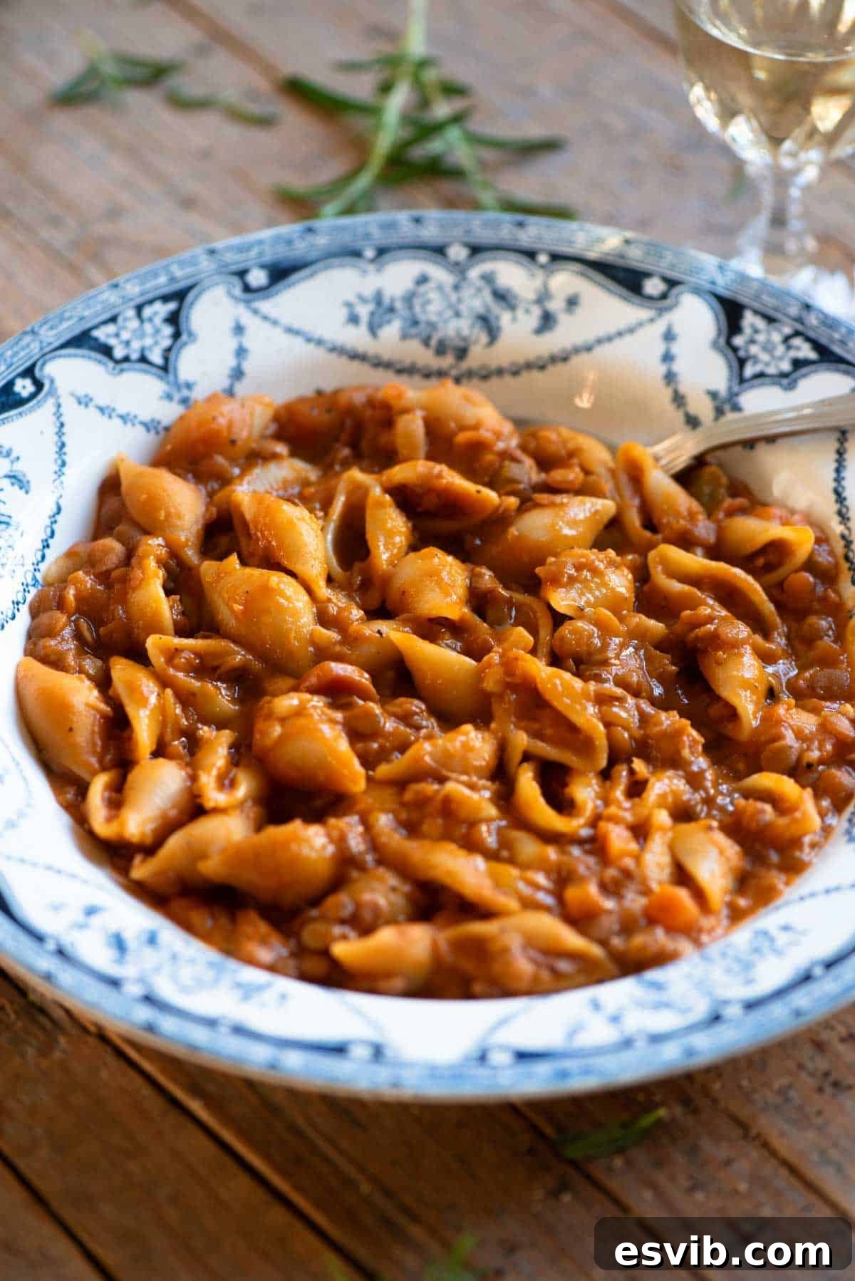 A close-up shot of steaming hot pasta and lentils, served in a charming blue vintage style bowl with a spoon, ready to be enjoyed.