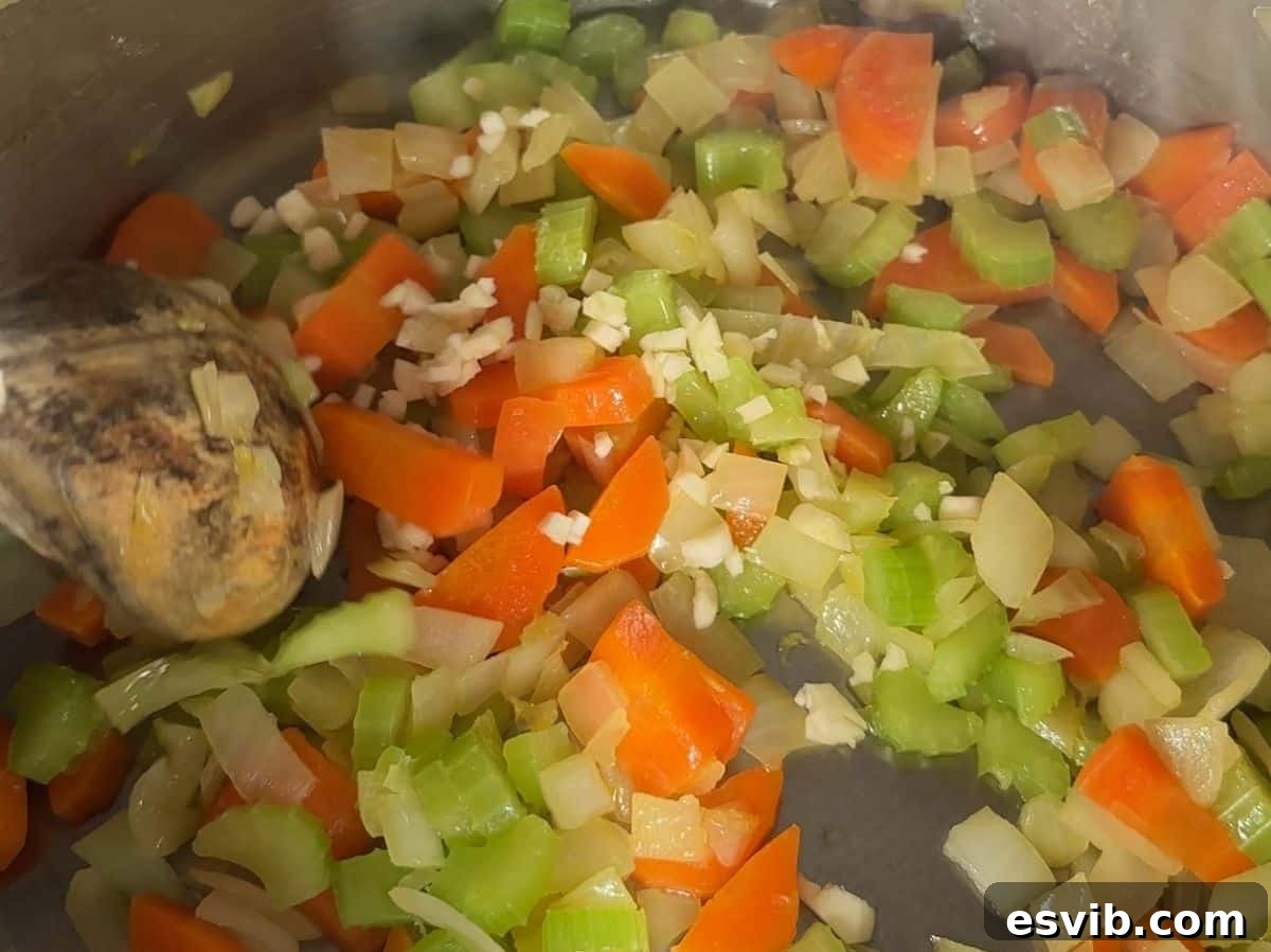 Soffritto (chopped onion, carrot, celery) sautéing in olive oil in a large pot, creating an aromatic base for the Acquacotta soup.