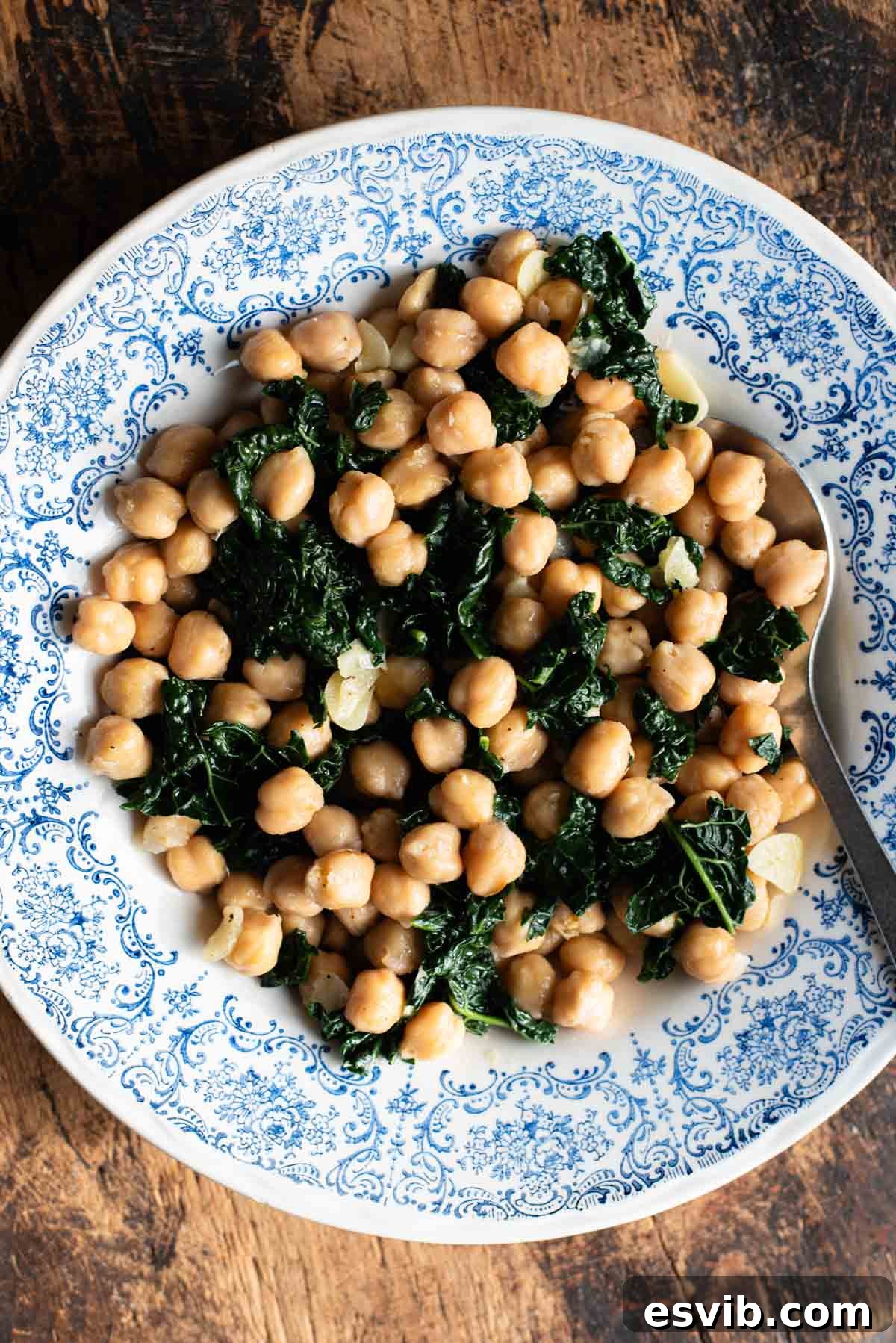 Chickpeas with garlic and cavolo nero in a blue and white bowl sitting on a rustic wooden surface.