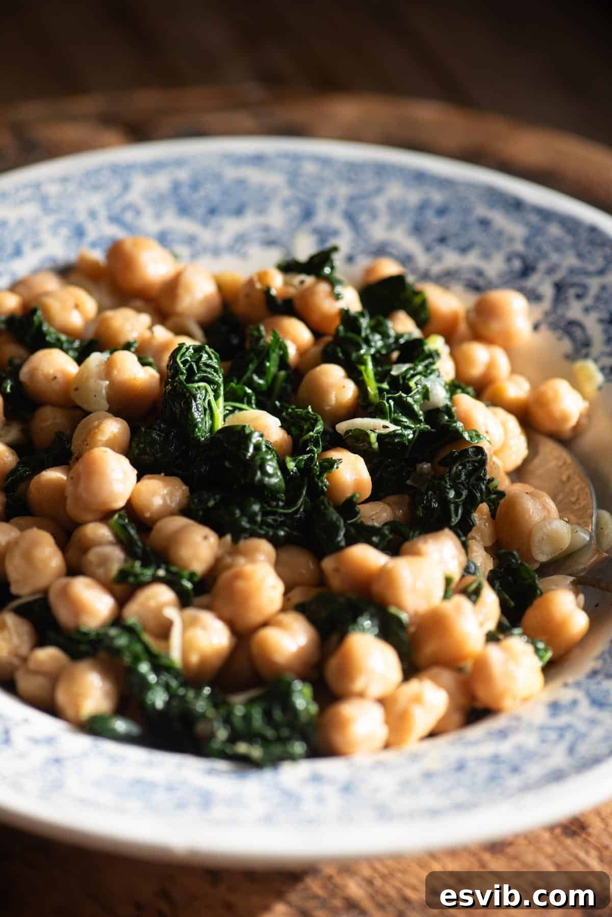 A close up of chickpeas and cavolo nero in a blue and white vintage style bowl sitting on a rustic wooden surface.