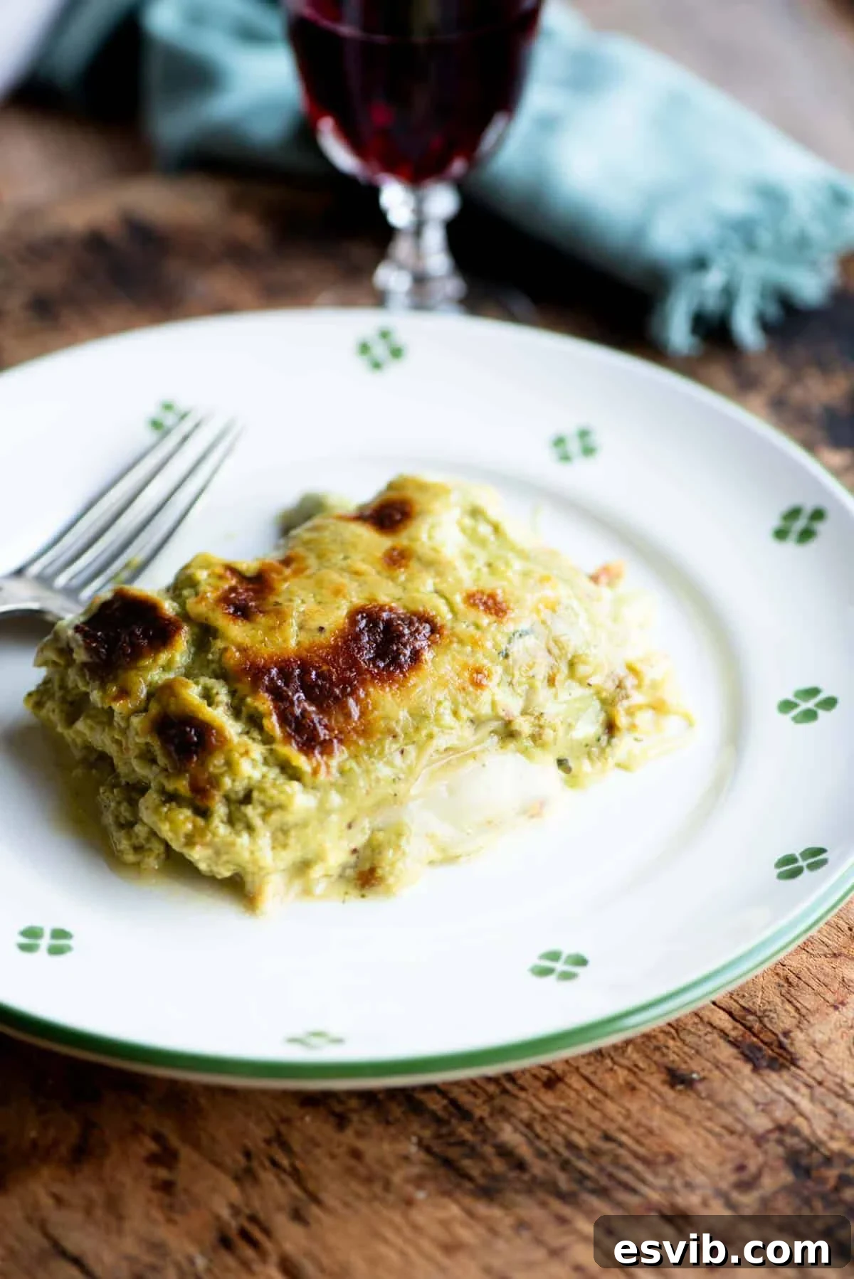 A slice of pistachio lasagna on a white plate with a fork at the side.
