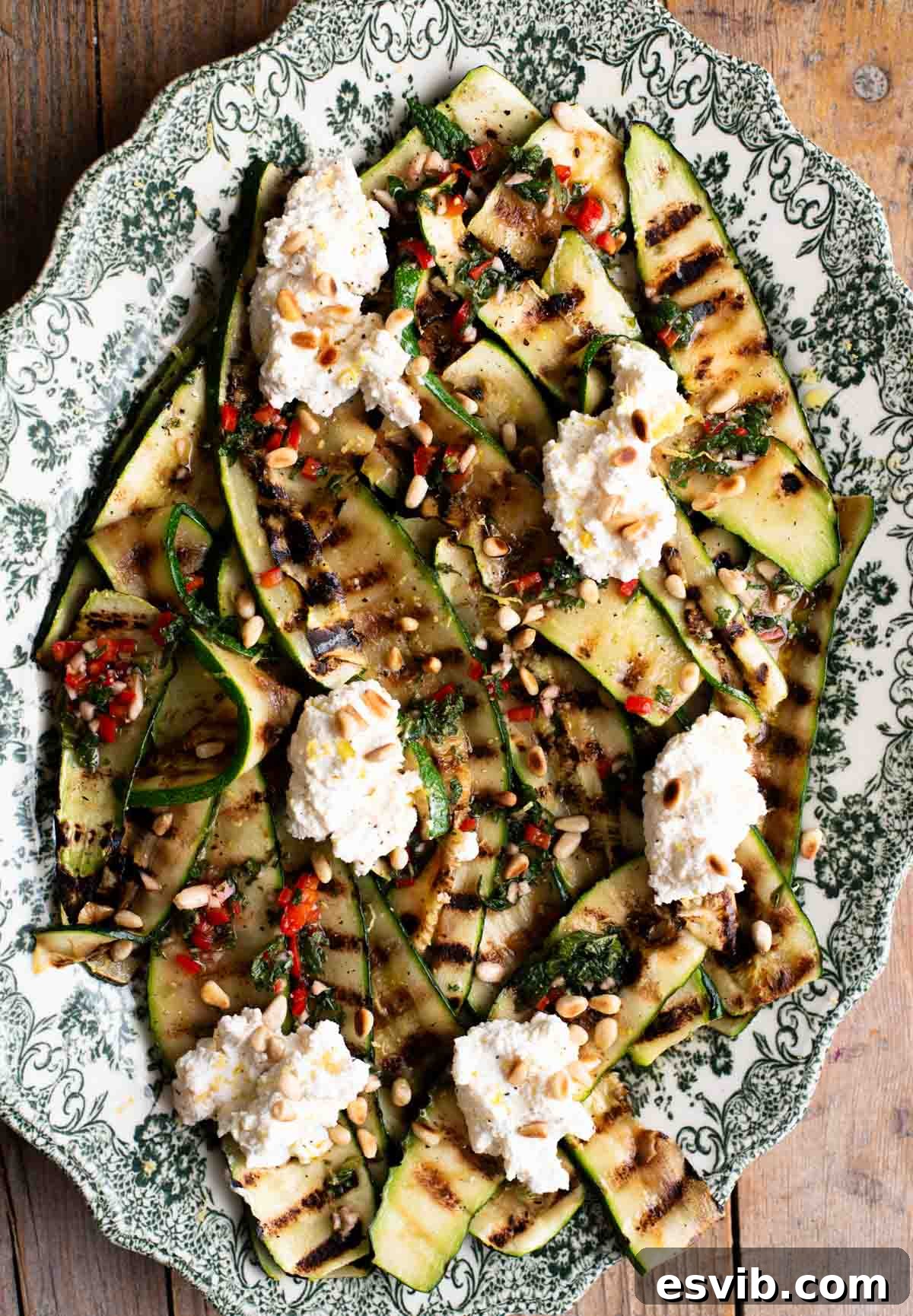 An overhead shot of grilled zucchini on a serving platter topped with garlic, chilli, mint and ricotta.