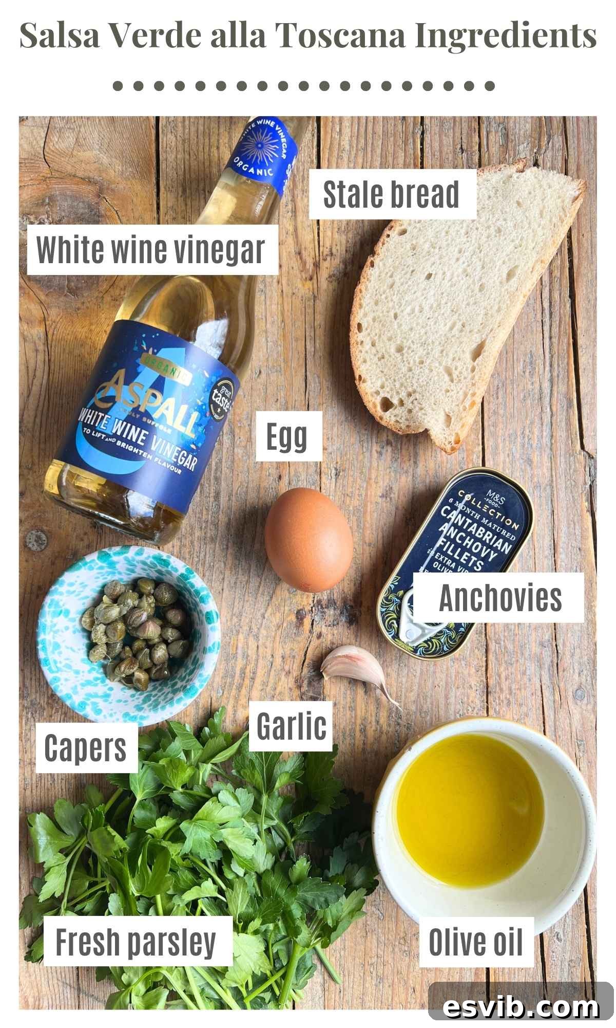 All the fresh ingredients required to prepare Tuscan salsa verde, beautifully arranged on a rustic wooden board, including white wine vinegar, stale bread, garlic, anchovies, a hard-boiled egg, capers, fresh parsley, and a bottle of olive oil.