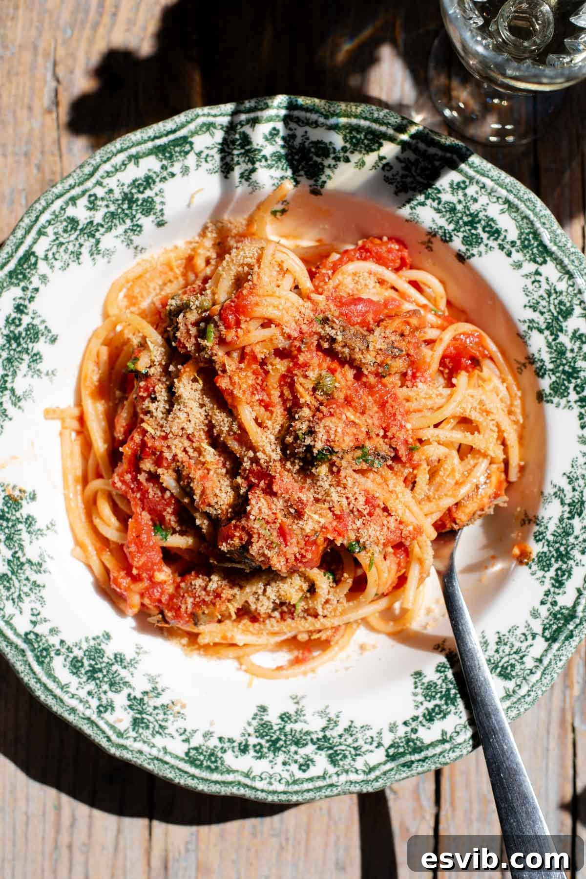 Golden Crumb Sardine and Tomato Pasta 2 An overhead shot of spaghetti in a tomato sauce with sardines and breadcrumbs on top, presented in a vintage style green and white bowl.