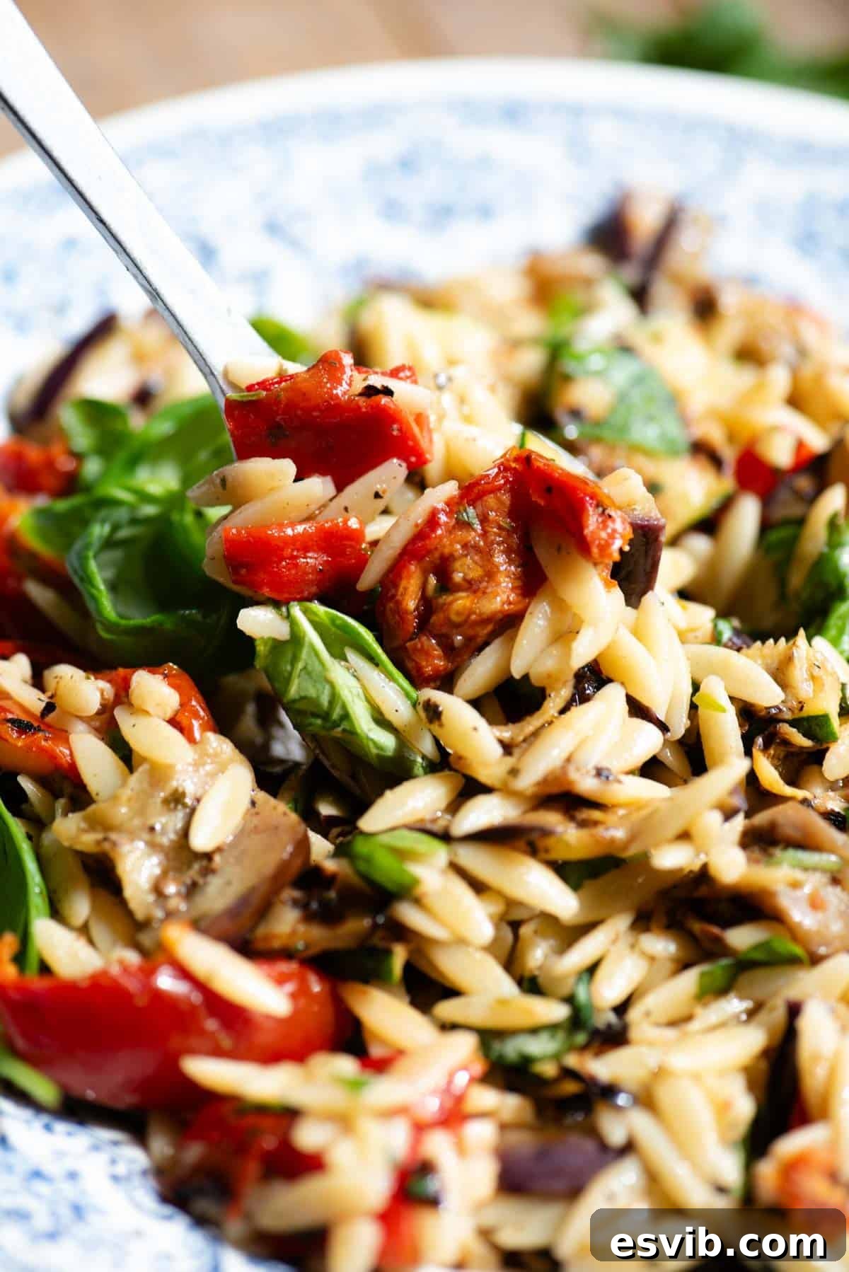A close up of an orzo pasta salad with tomatoes and grilled veg.