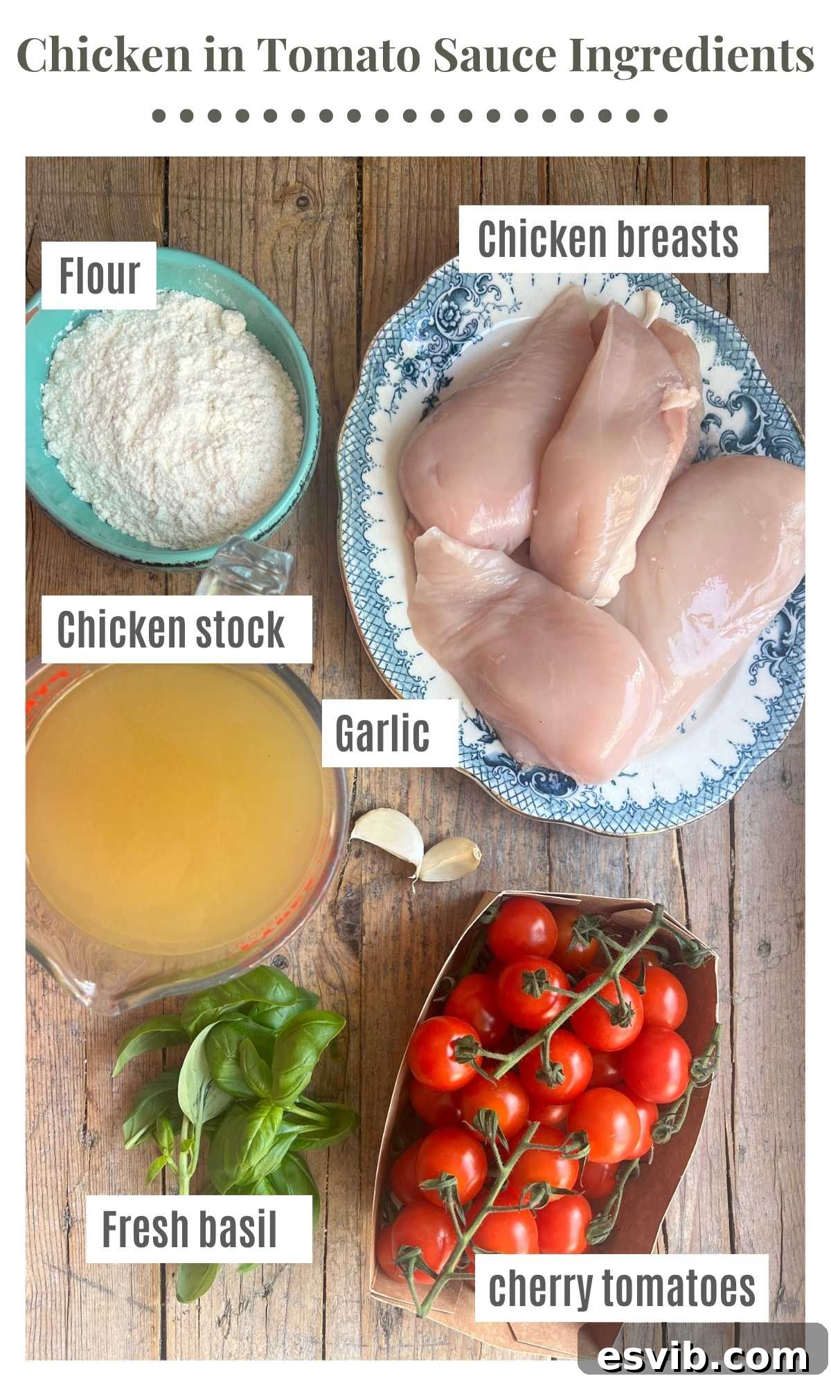 An overhead shot showing ingredients laid out on a rustic wooden board. The ingredients are labelled; flour, chicken breasts, cherry tomatoes, chicken stock, fresh basil, garlic. 