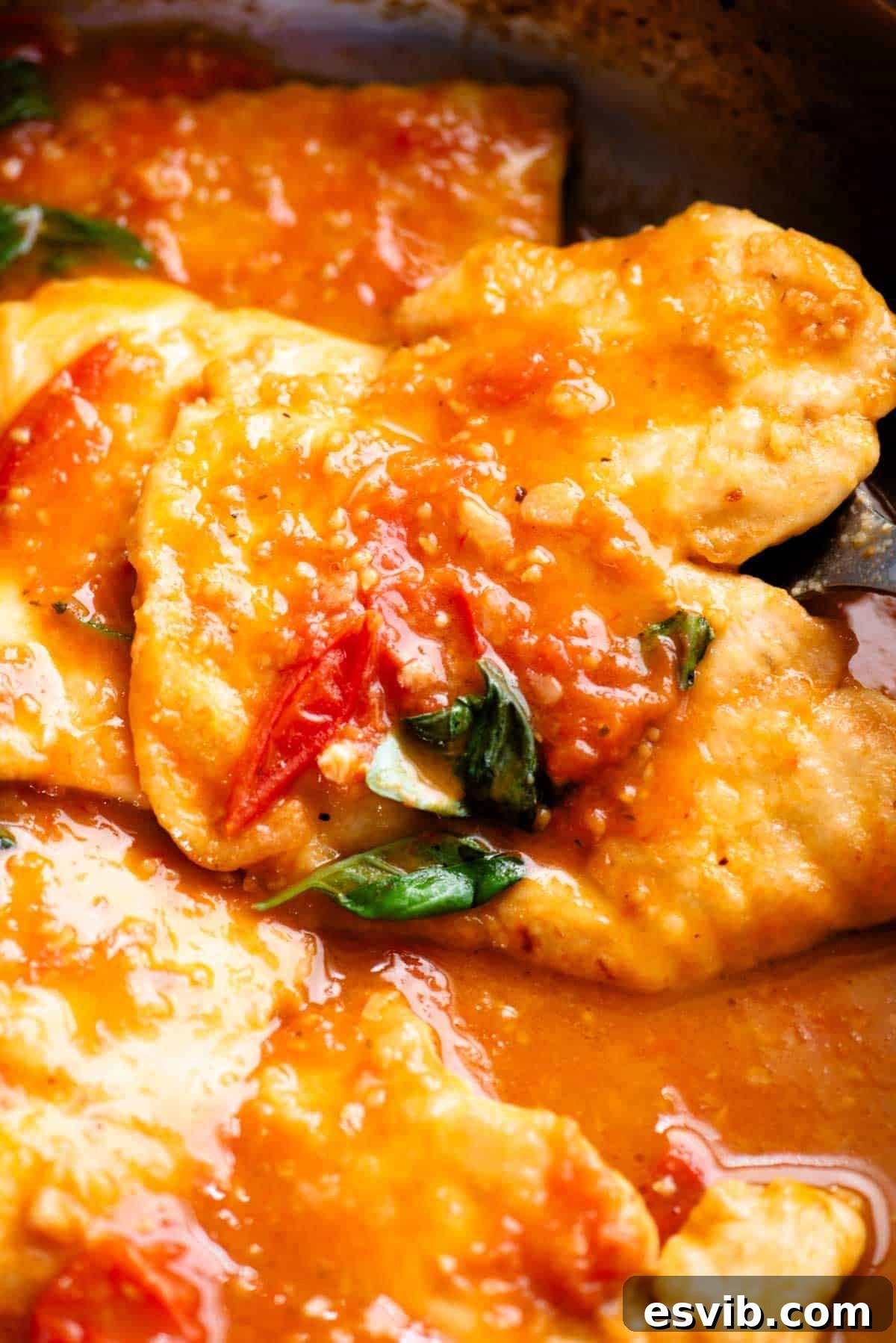A close up of a piece on chicken in a pan covered in tomato and basil sauce.