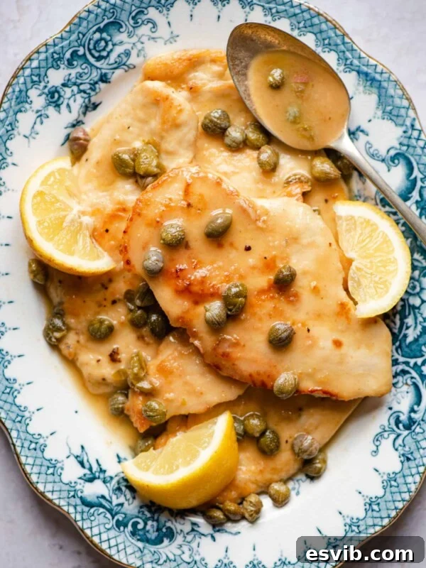 An overhead shot of chicken piccata on a blue serving plate with lemon wedges and capers